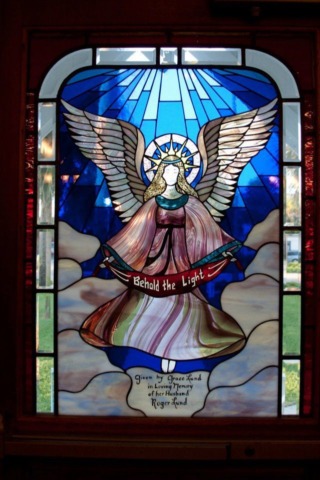 A stained glass window with an angel holding a banner that says hold the light