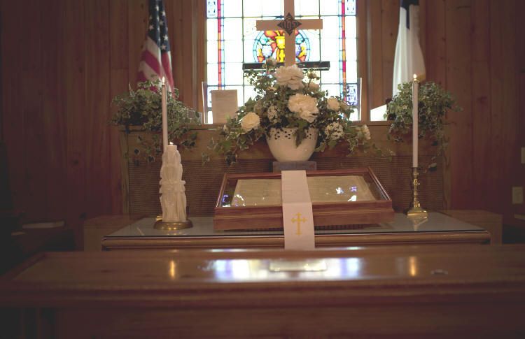 A church altar with flowers , candles , a cross and an american flag.