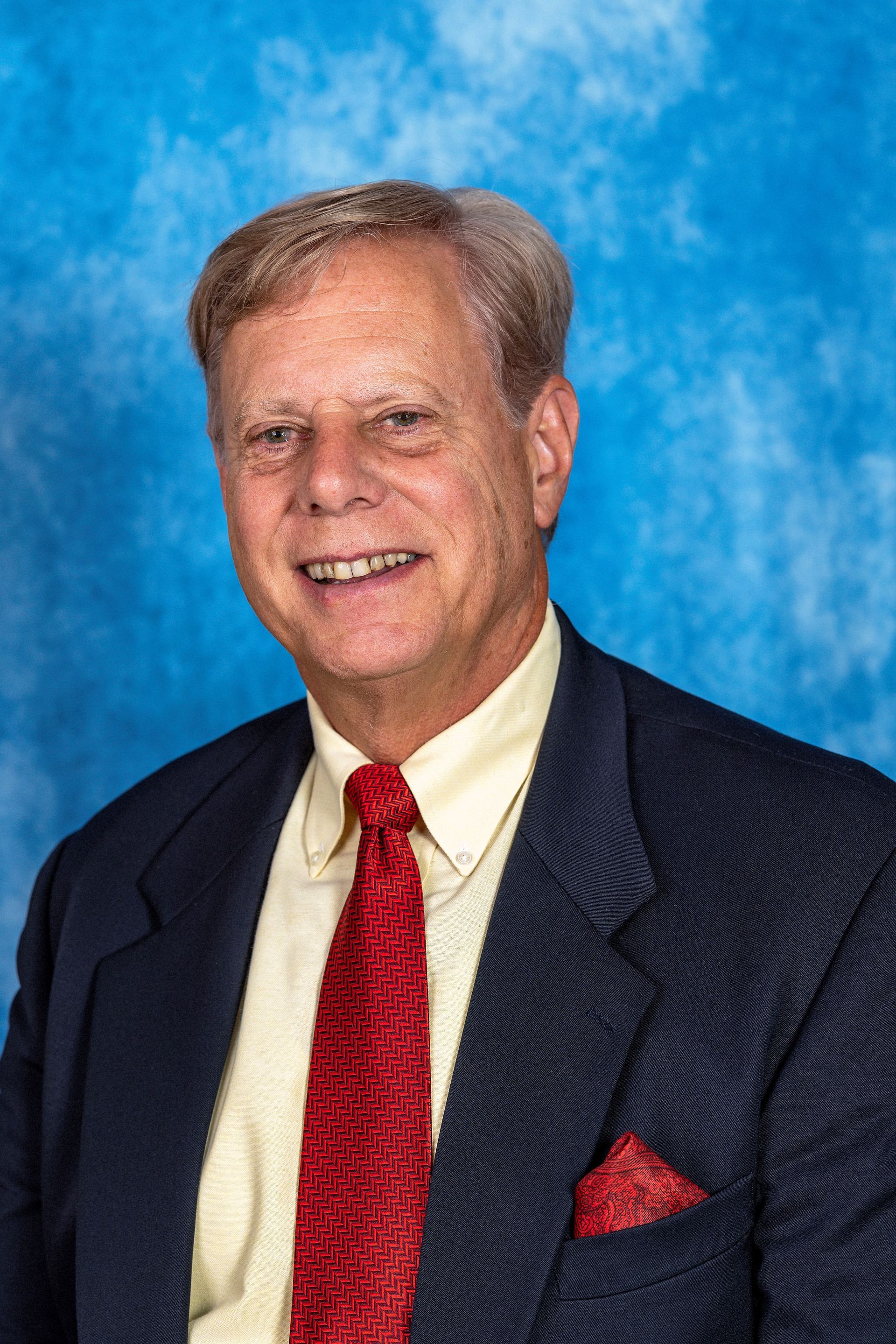 A man in a suit and tie is smiling in front of a blue background