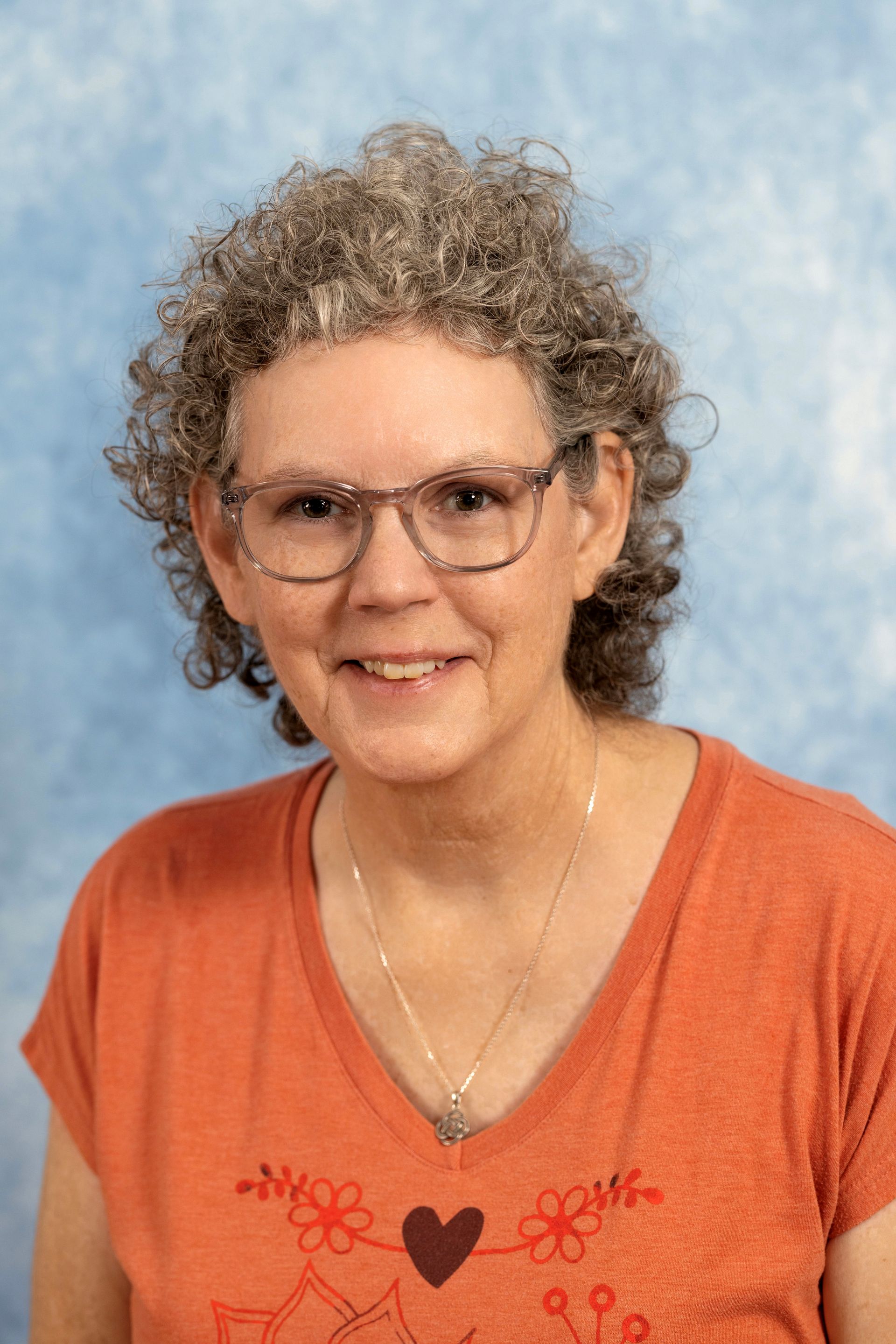 A woman wearing glasses and an orange shirt with a heart on it