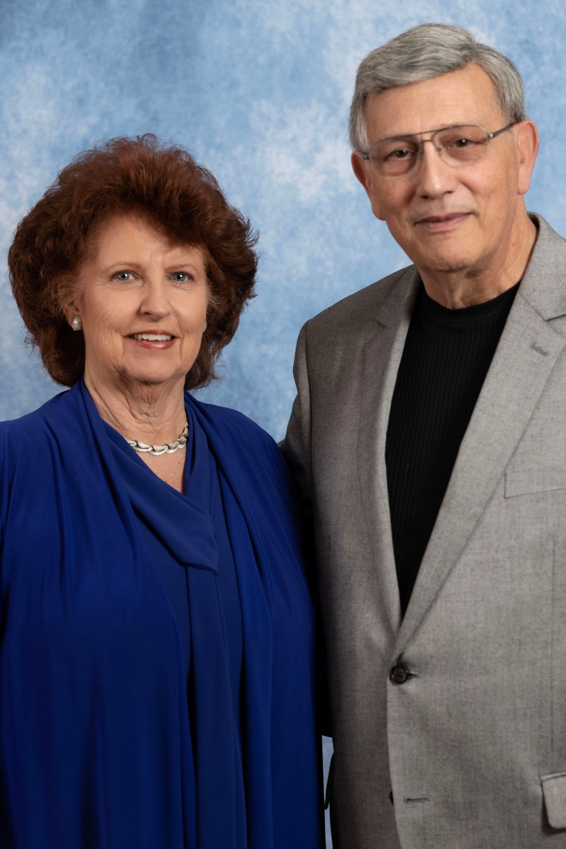 A man in a suit and a woman in a blue dress are posing for a picture.