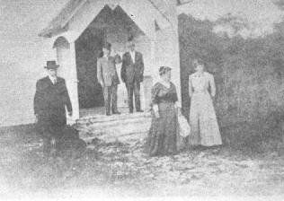 A black and white photo of a group of people standing in front of a church.
