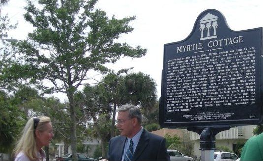 A man and woman are standing in front of a sign that says myrtle cottage