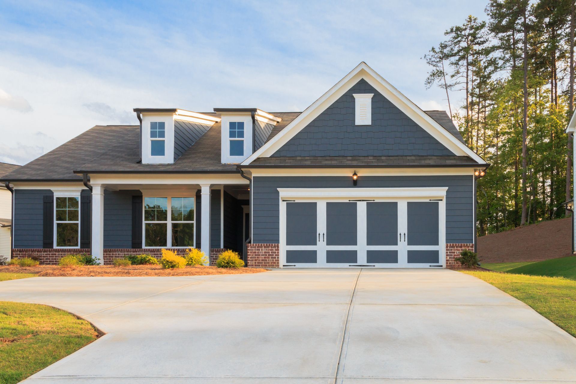Blue house with white trim, brick accents, and a concrete driveway on a sunny day.
