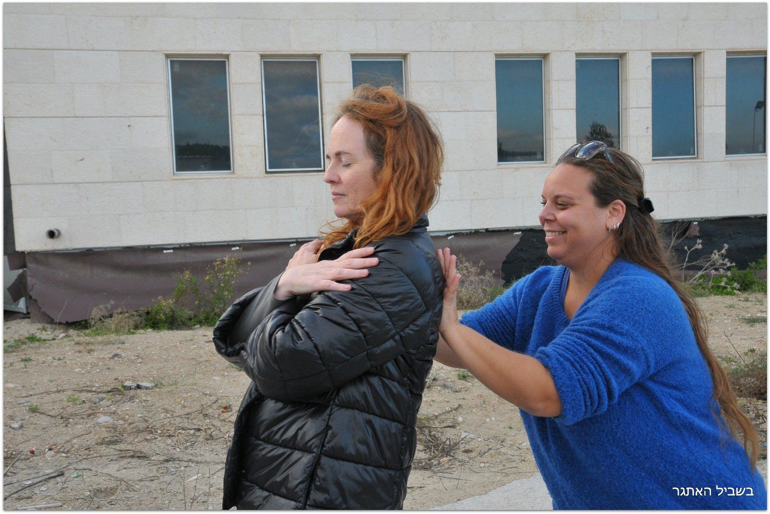 אישה בסוודר כחול מניחה את ידיה על חזה של אישה אחרת