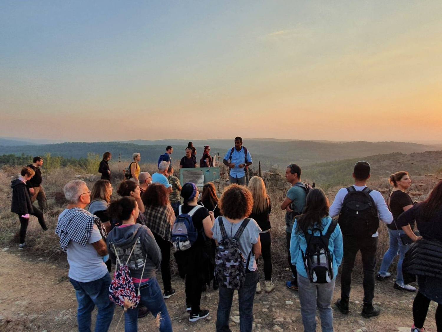 קבוצה של אנשים עומדת על ראש גבעה בשקיעה.