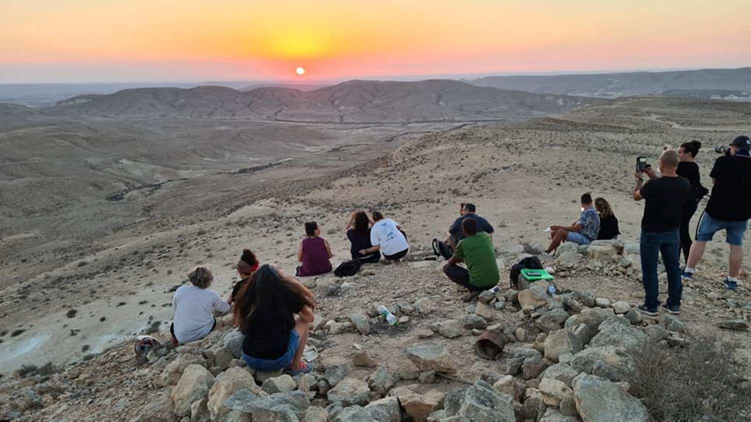 קבוצה של אנשים יושבת על ראש גבעה סלעית וצופה בשקיעה.