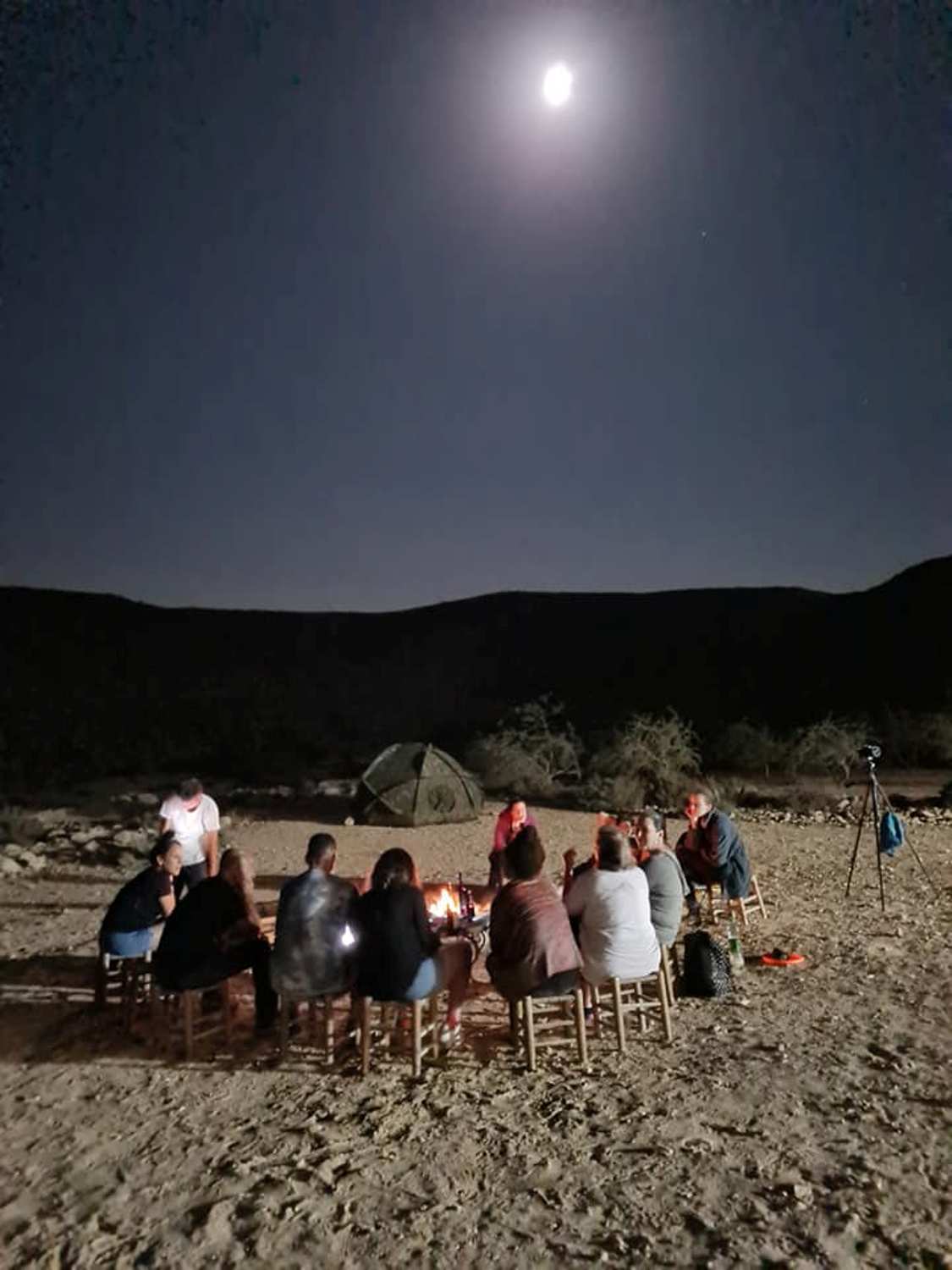קבוצת אנשים יושבת סביב מדורה במדבר בלילה.