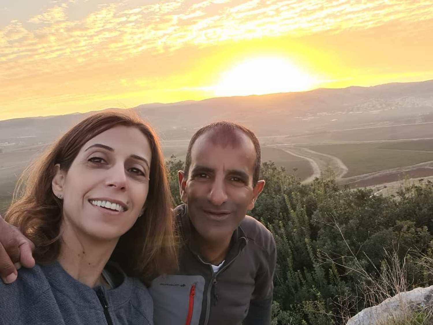גבר ואישה מצטלמים על ראש גבעה בשקיעה.