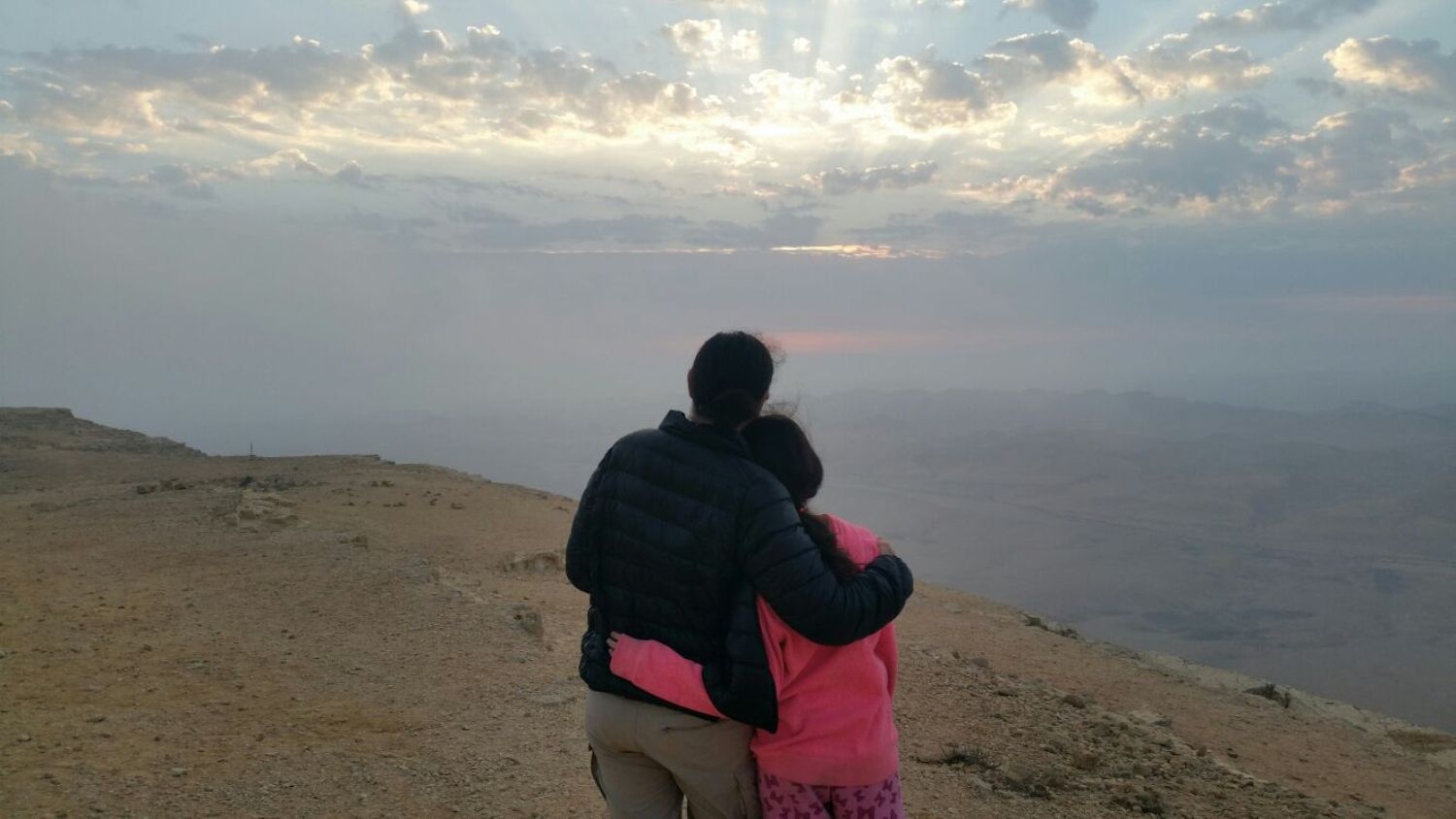 גבר ואישה מחבקים זה את זה בזמן שהם עומדים על ראש גבעה.