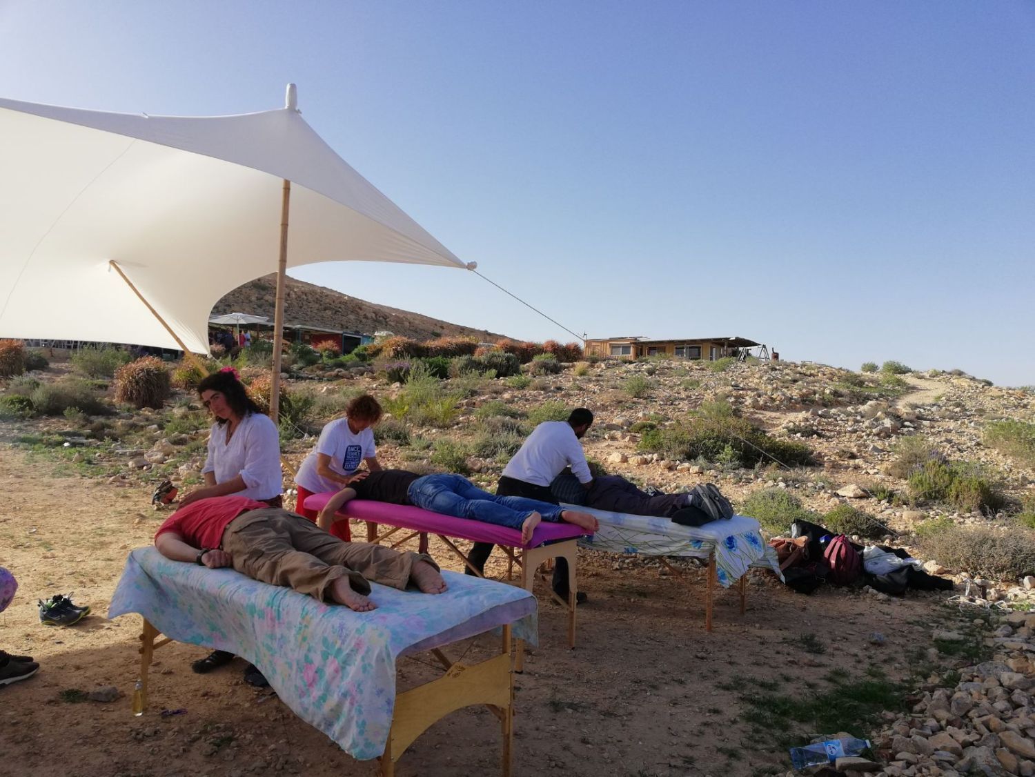 קבוצה של אנשים מקבלים עיסויים במדבר מתחת למטריה.