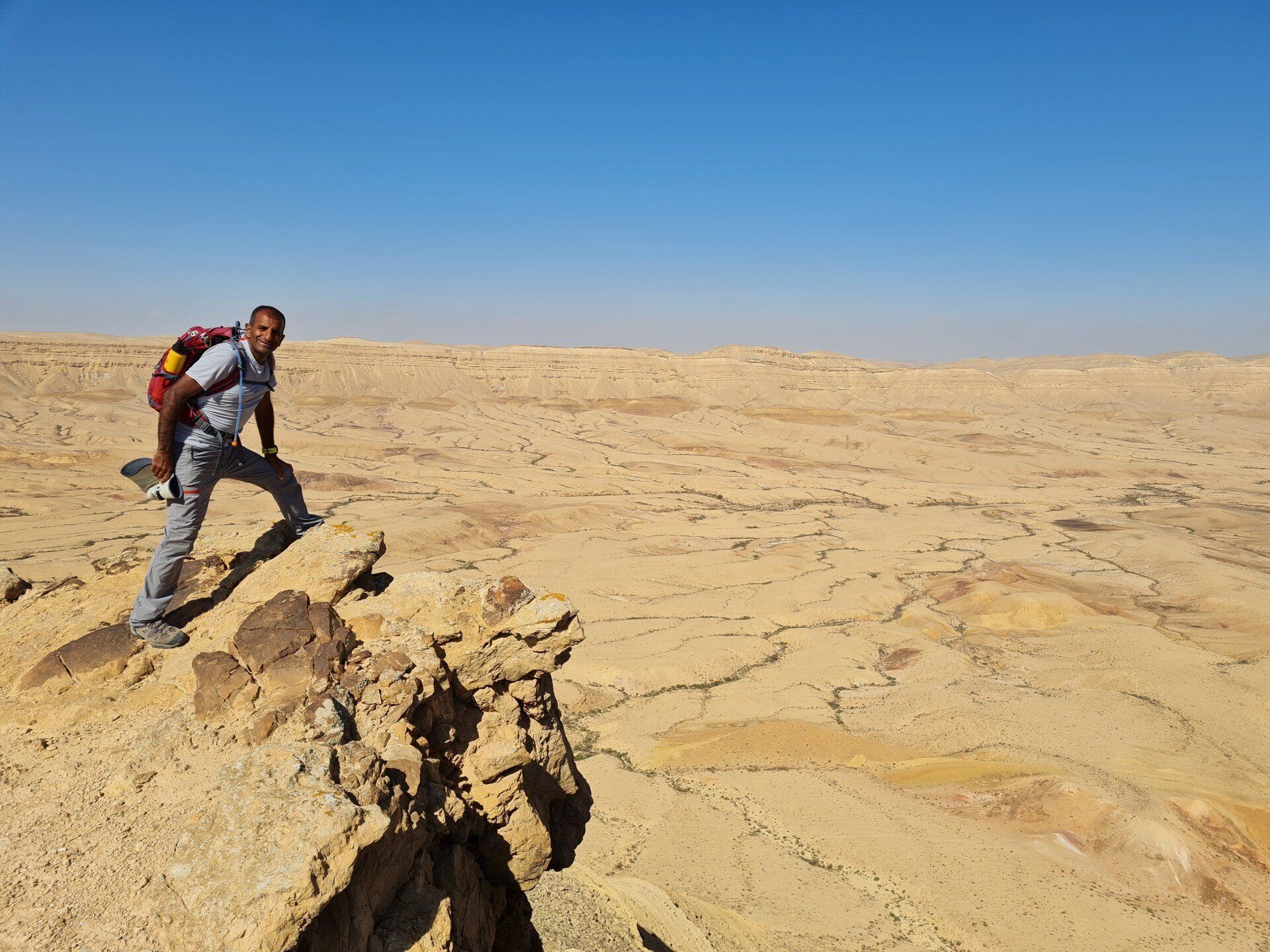 אדם עם תרמיל עומד על גבי סלע במדבר.
