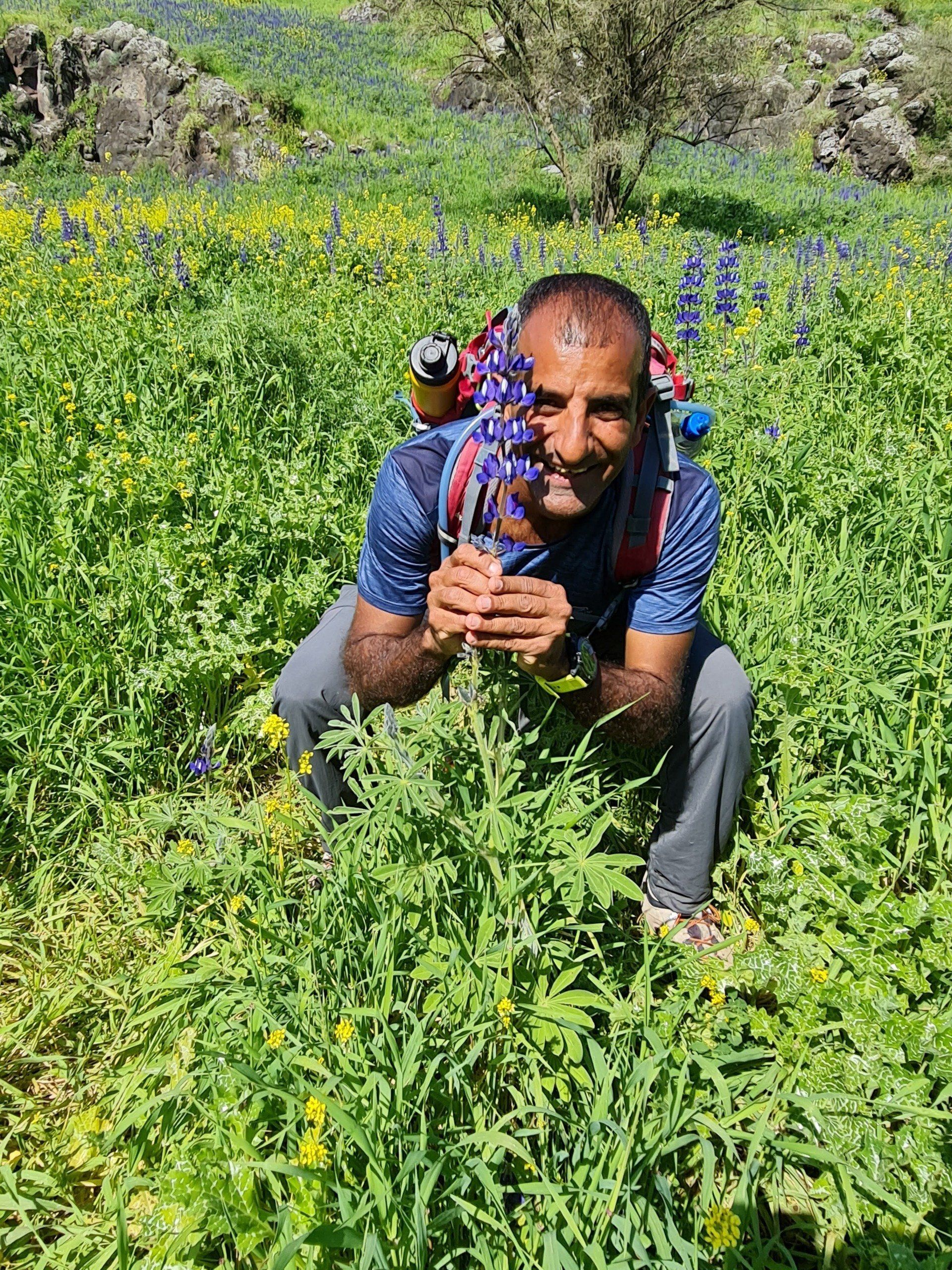 גבר כורע בשדה פרחים אוחז בפרח.