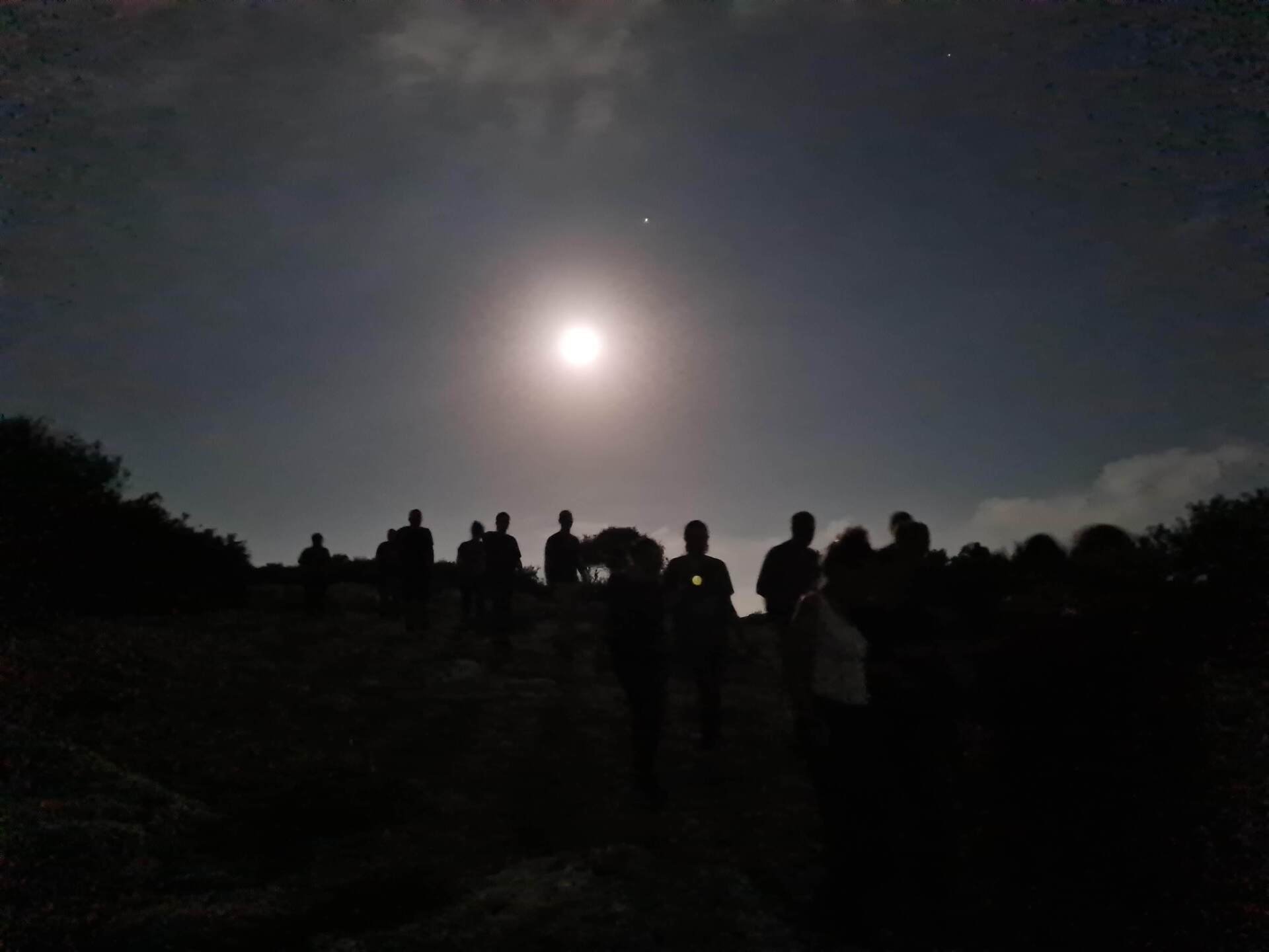 קבוצת אנשים עומדת מול ירח מלא.