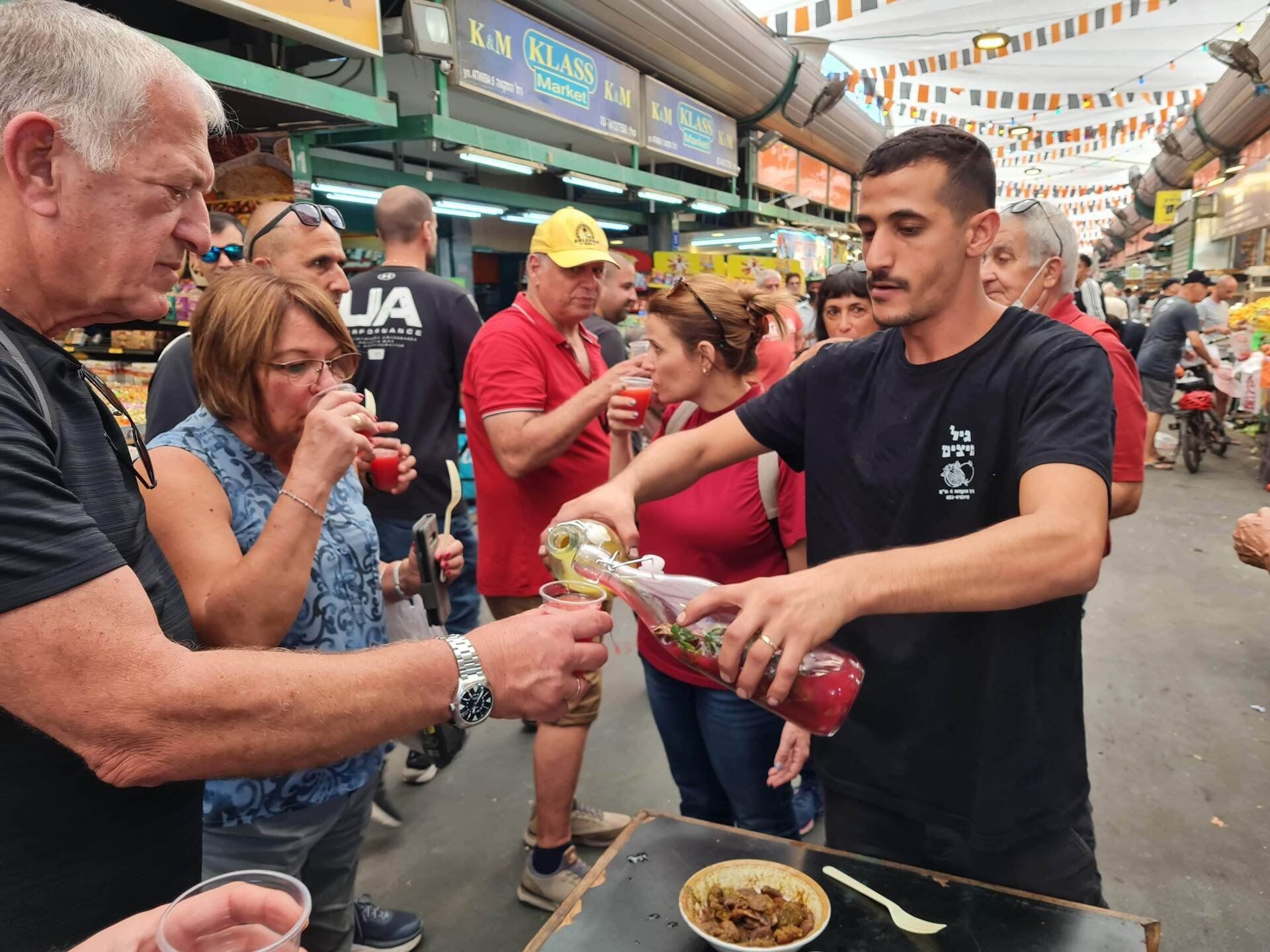אדם מוזג משקה לכוס עבור קבוצת אנשים.