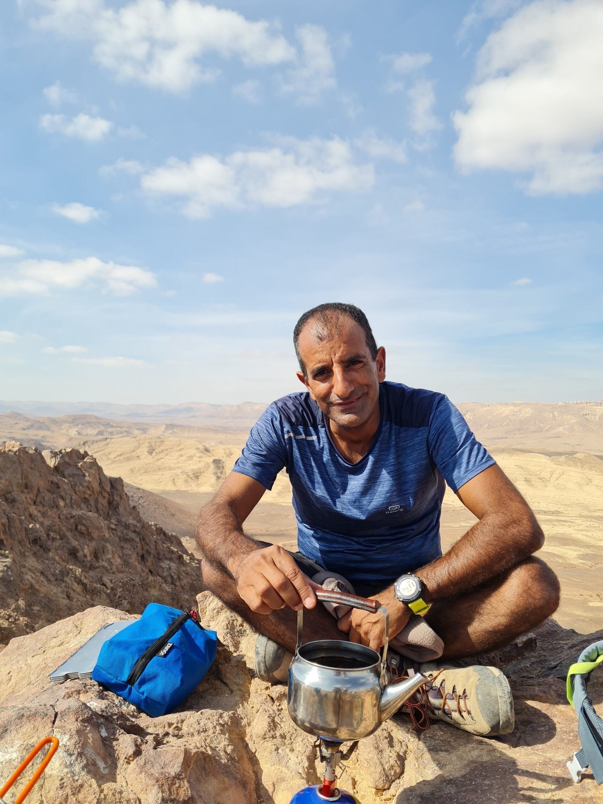 איש יושב על גבי סלע עם קומקום בידו.