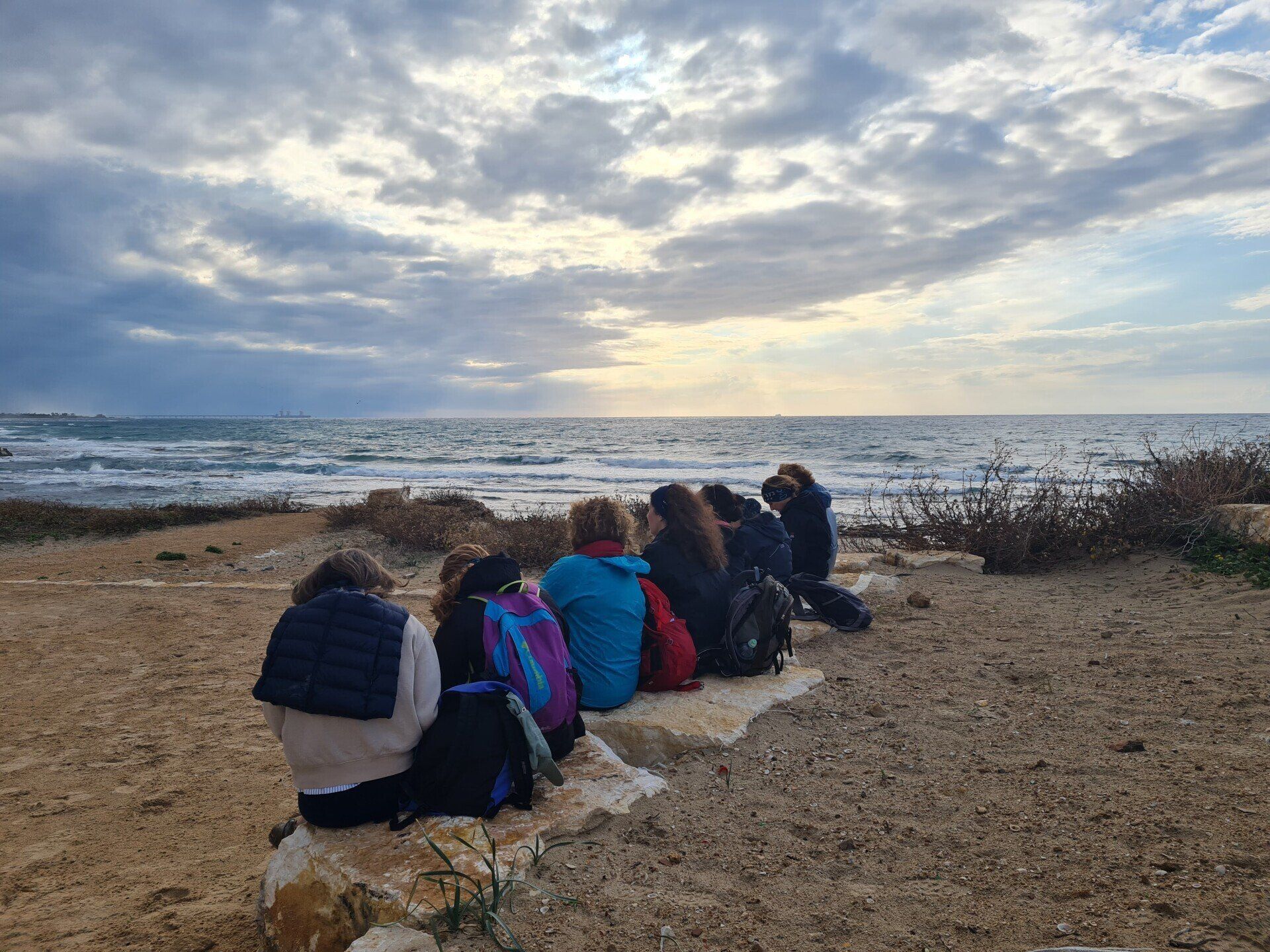 קבוצה של אנשים יושבת על סלעים על החוף ומסתכלת על האוקיינוס.