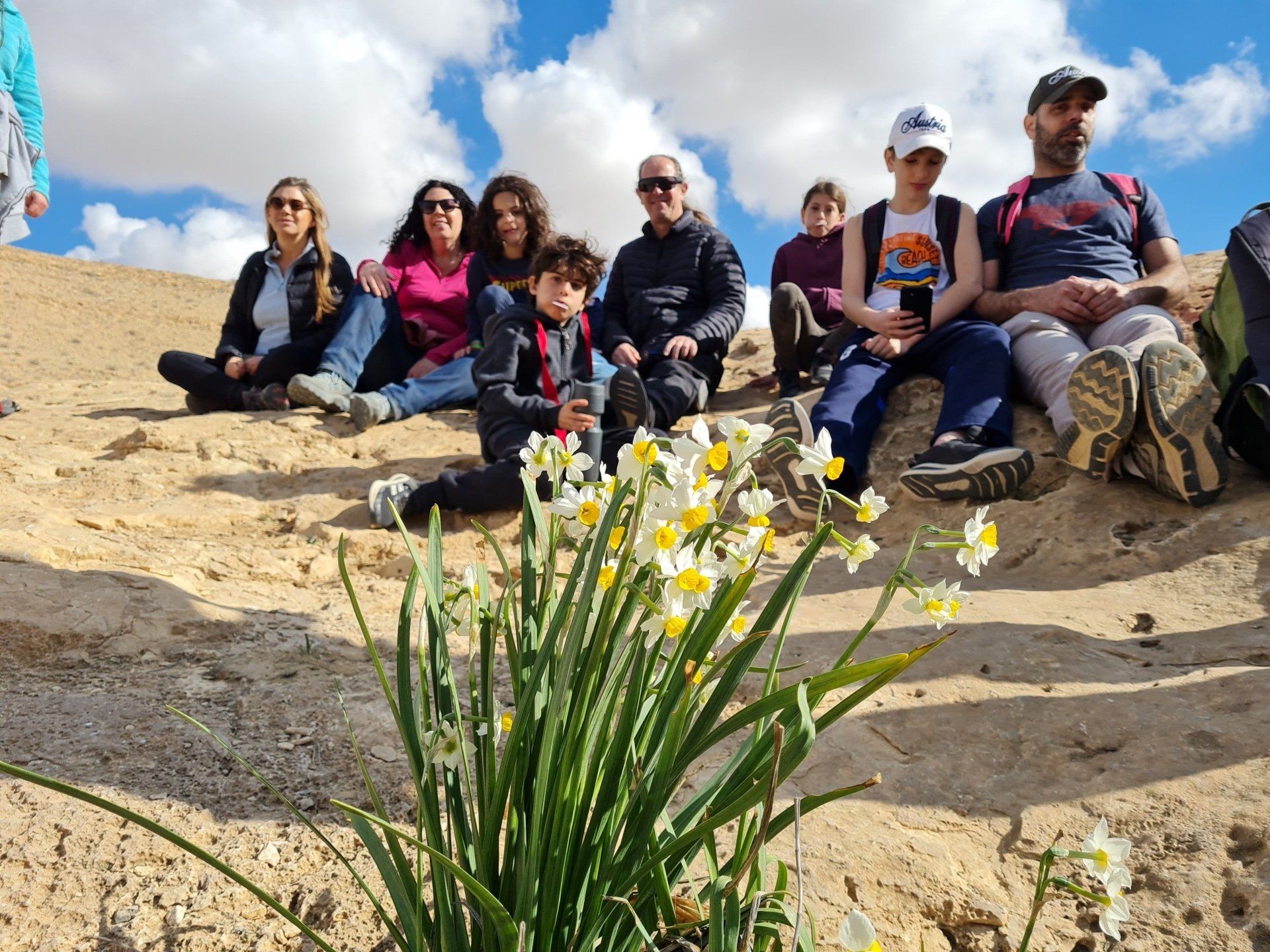 קבוצת אנשים יושבת על גבי דיונת חול עם פרחים בחזית.