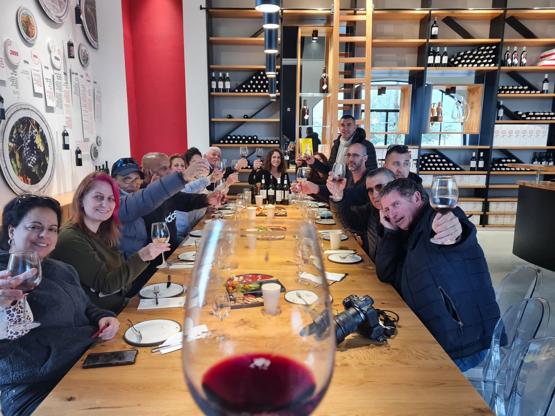 קבוצה של אנשים יושבת ליד שולחן ארוך וצולים עם כוסות יין.