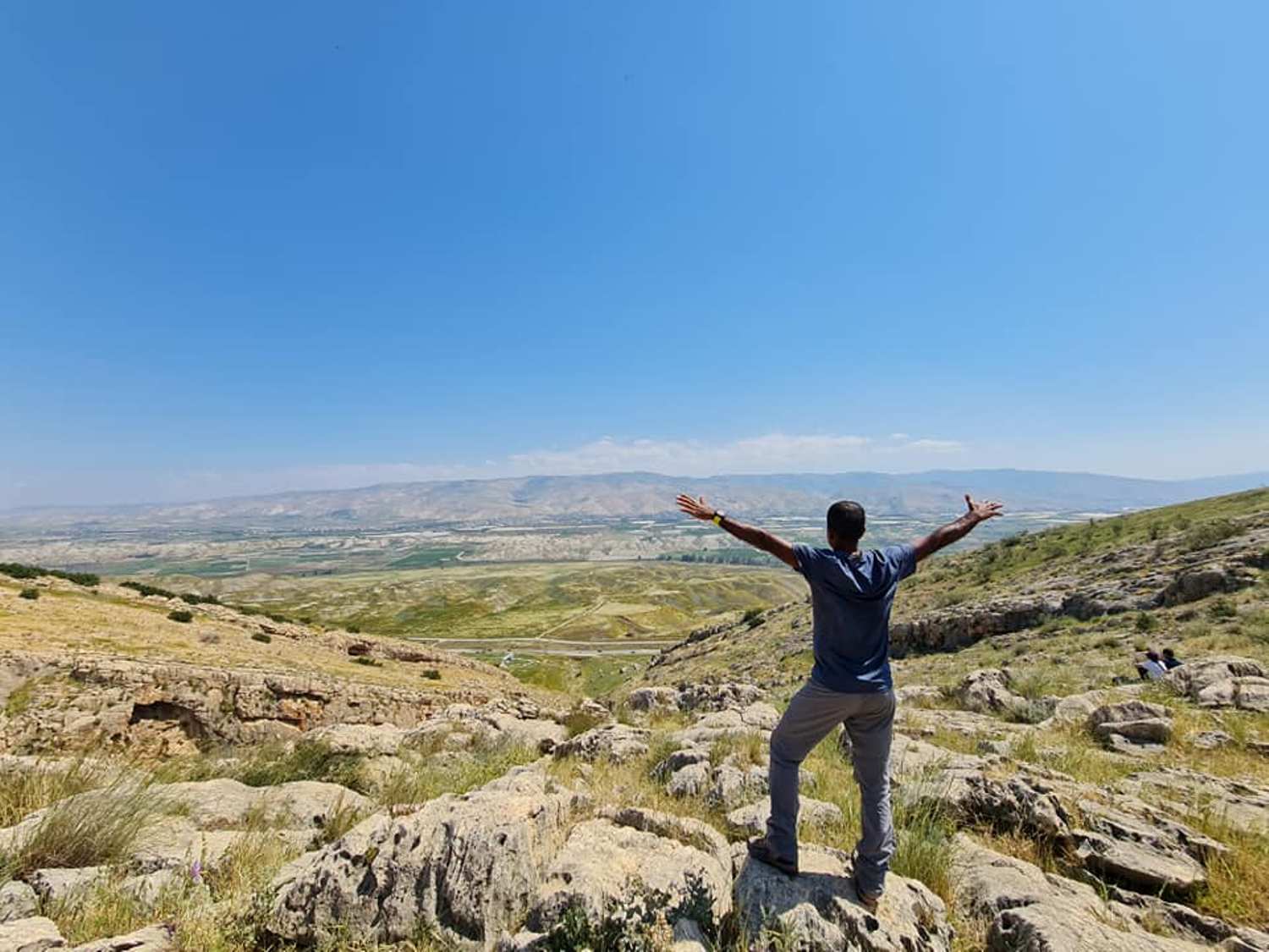אדם עומד על ראש גבעה סלעית עם זרועותיו פרושות.