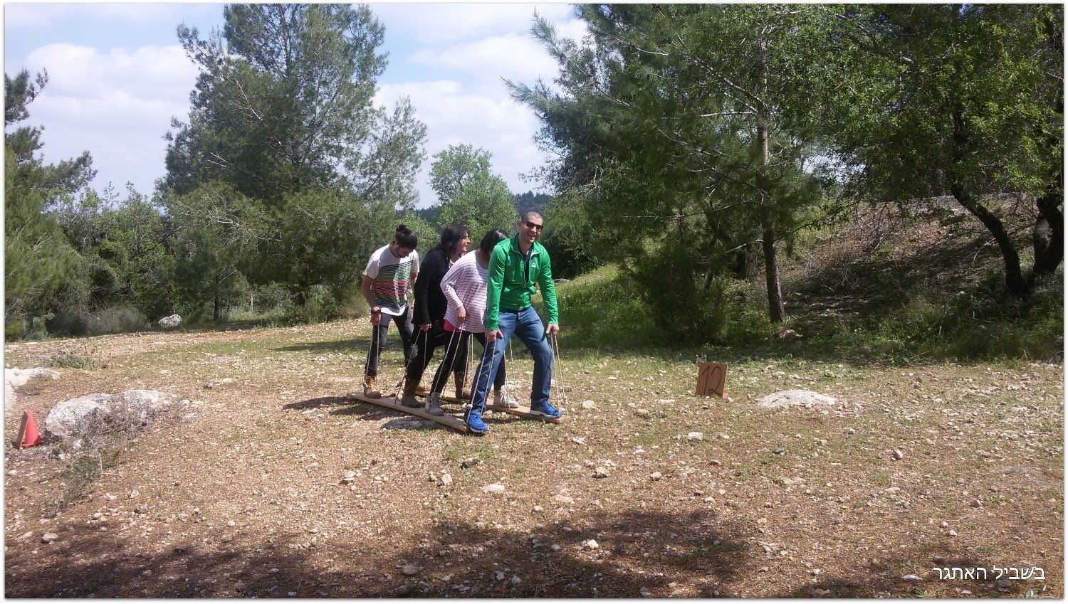 קבוצת אנשים עומדת בשדה עם עצים ברקע.