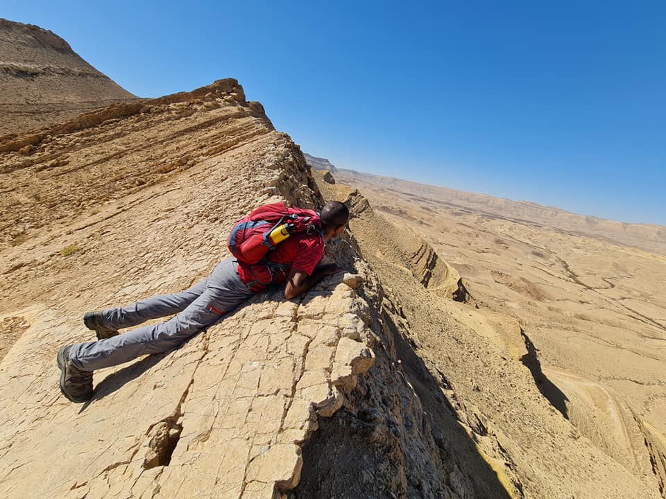 אדם שוכב על ראש צוק סלעי במדבר.