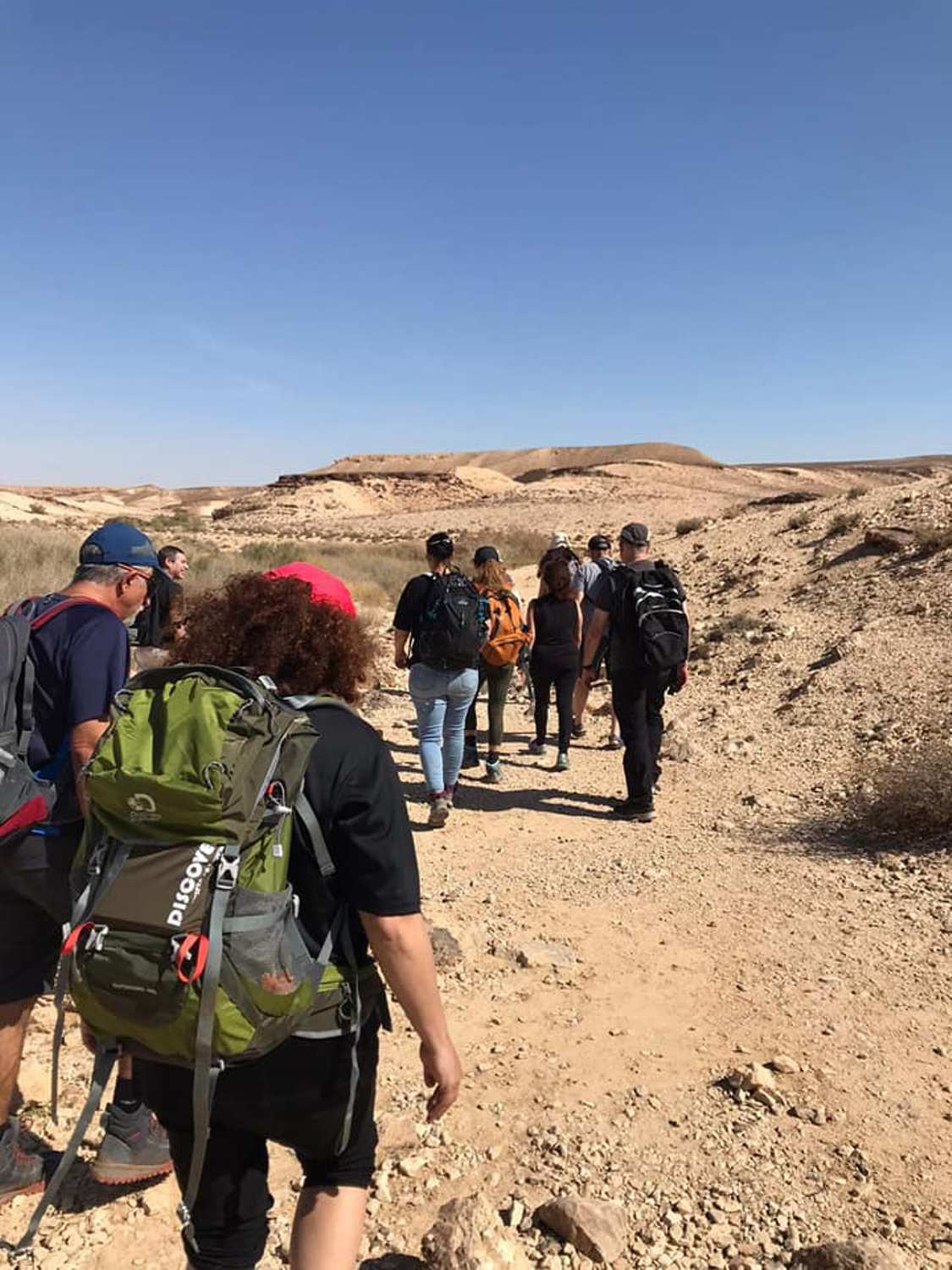 קבוצה של אנשים עם תרמילים הולכים בדרך עפר.