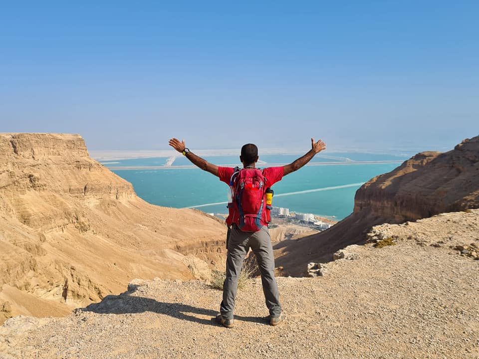 גבר עם תרמיל עומד על ראש גבעה עם זרועותיו פרושות.