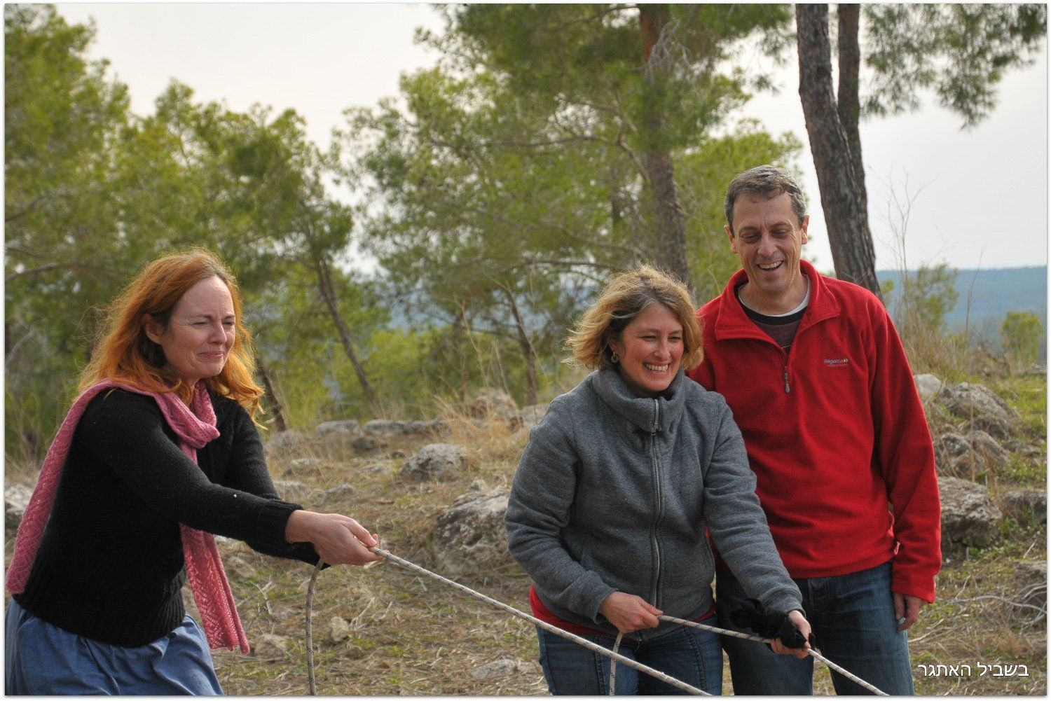 גבר ושתי נשים מושכים חבל בשדה.