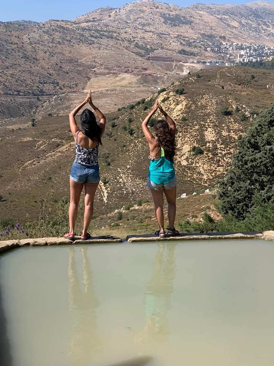 שתי נשים עומדות על שפת בריכה עם הרים ברקע.