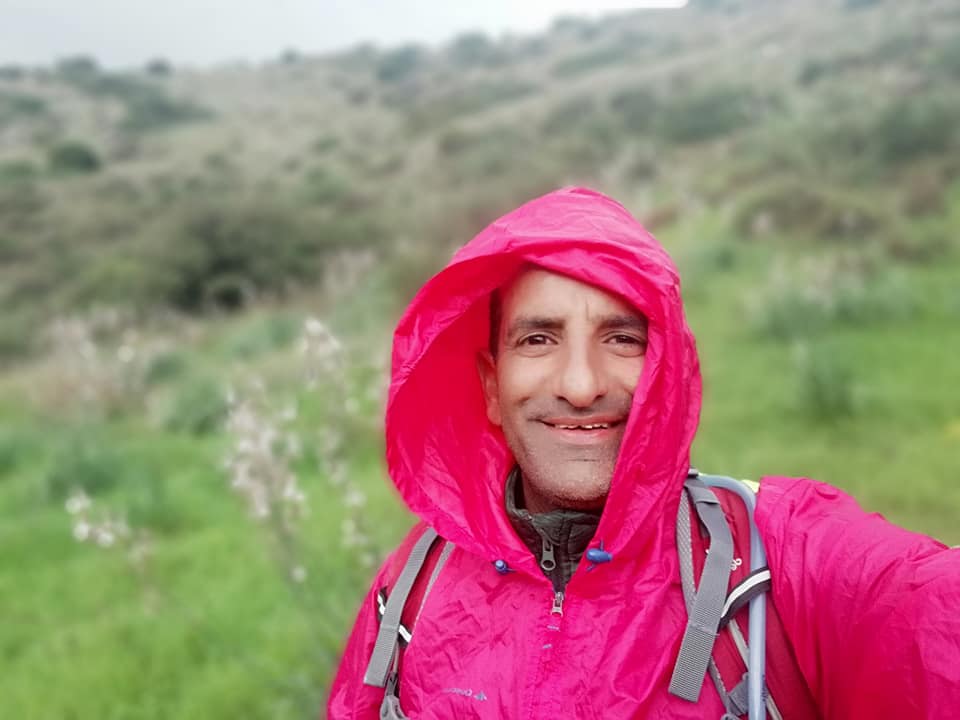 גבר שלובש מעיל גשם ורוד מצלם סלפי בשדה.