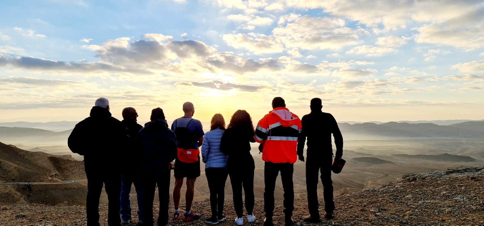 קבוצה של אנשים עומדת על ראש גבעה ומסתכלת על השקיעה.