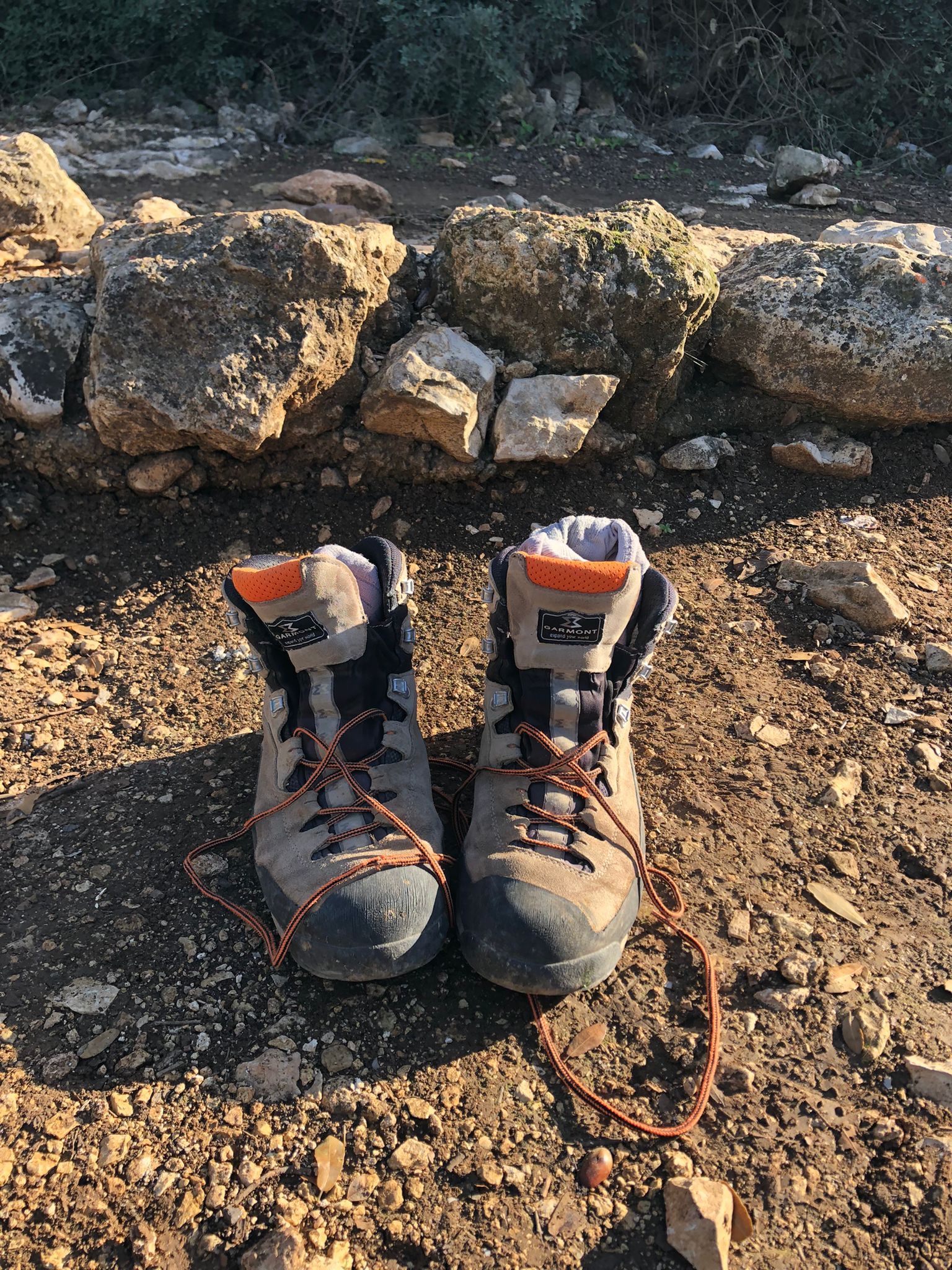 זוג נעלי הליכה יושבים על האדמה ליד קיר סלע.