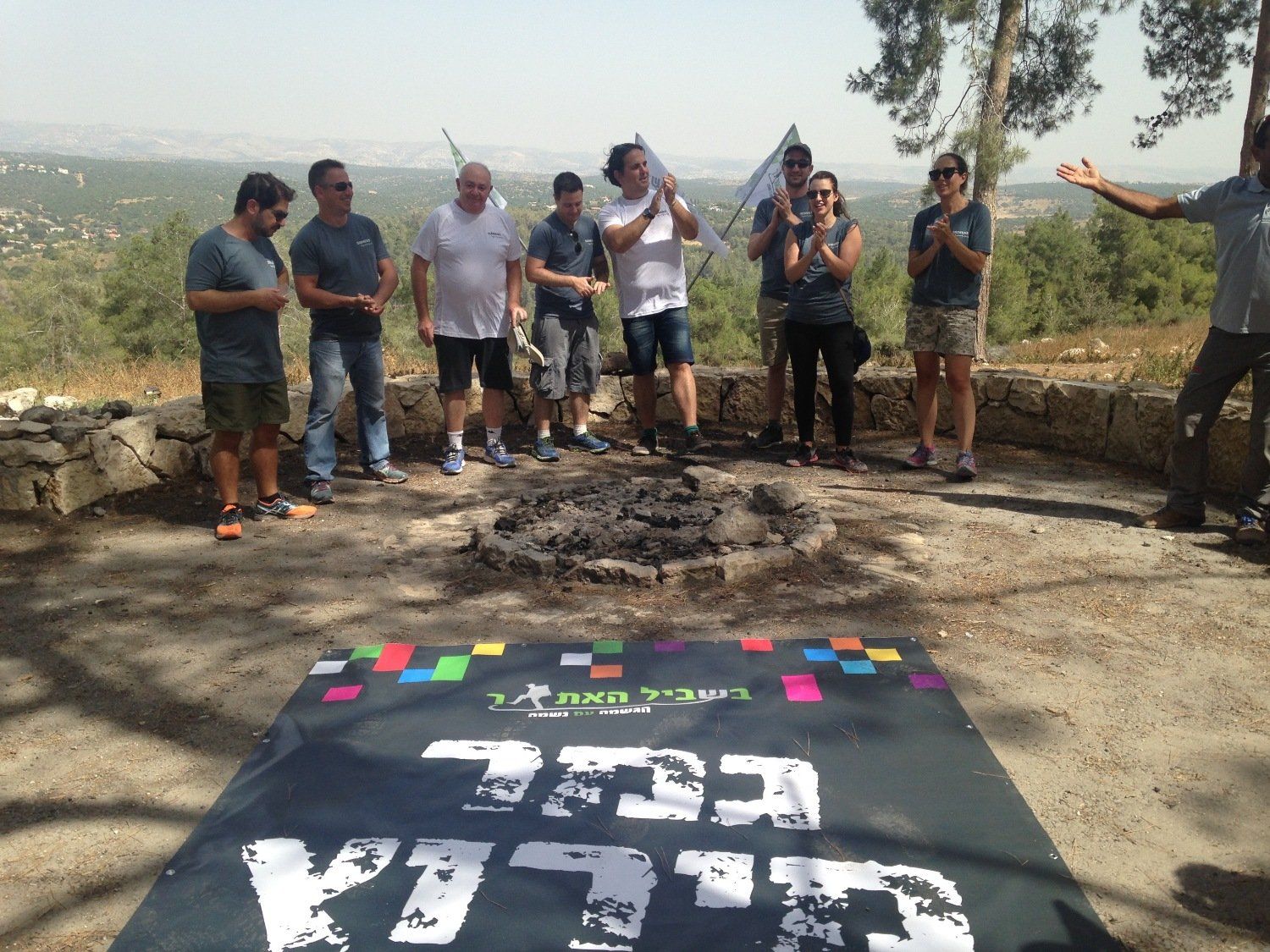 קבוצת אנשים עומדת מסביב לשלט שכתוב עליו 'א'