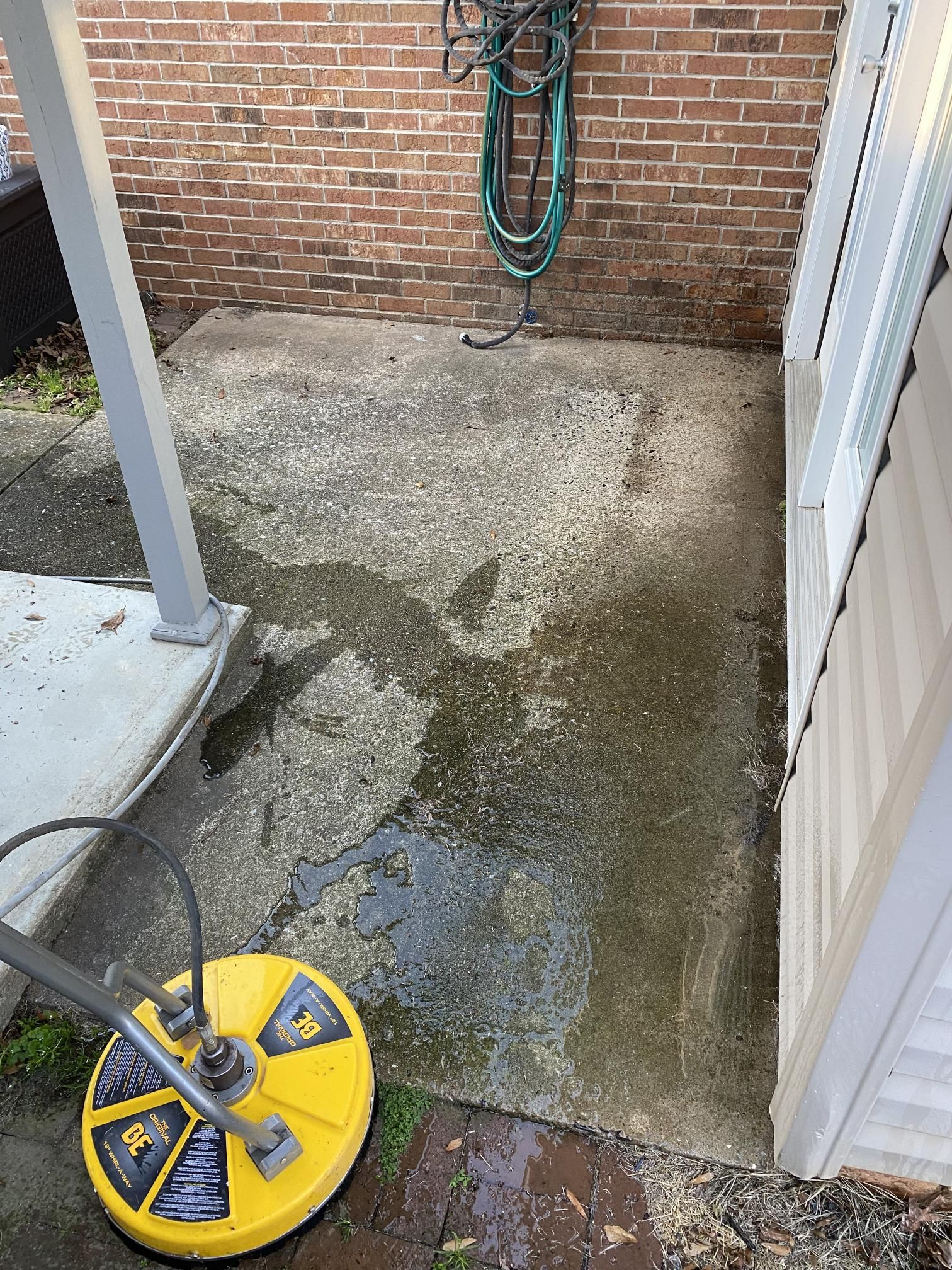 A yellow pressure washer is sitting on a concrete patio next to a brick wall.