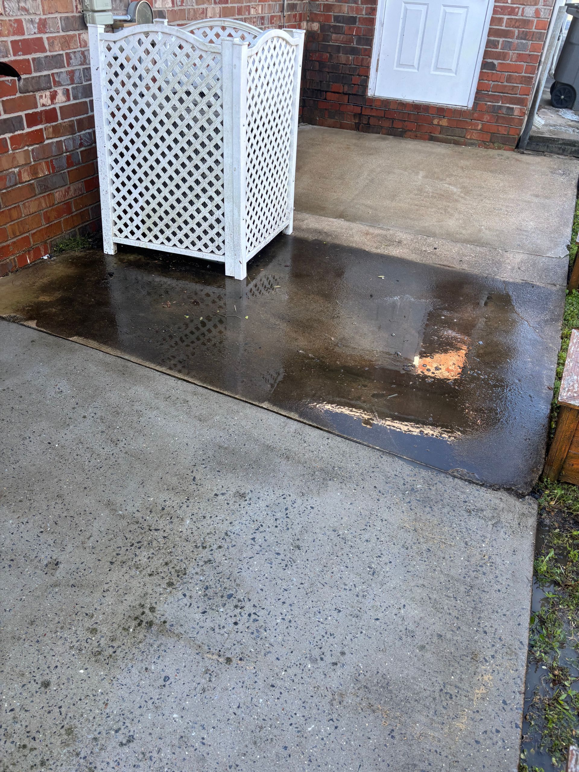 Wet concrete patio with a white lattice screen, brick wall and door.