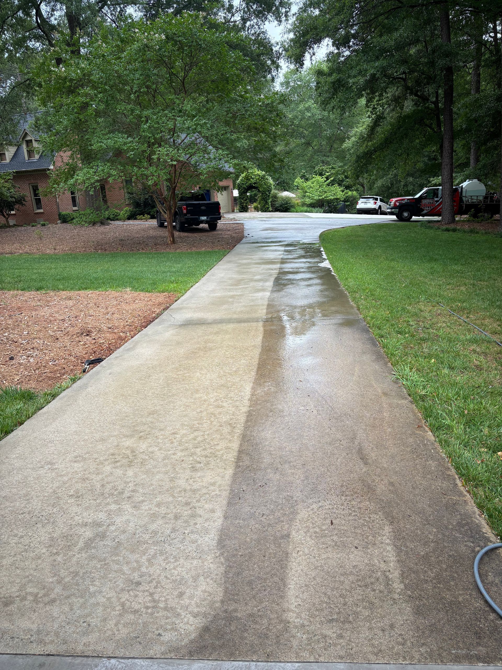 Driveway being pressure washed; half cleaned, half dirty. Outdoors, light gray concrete.