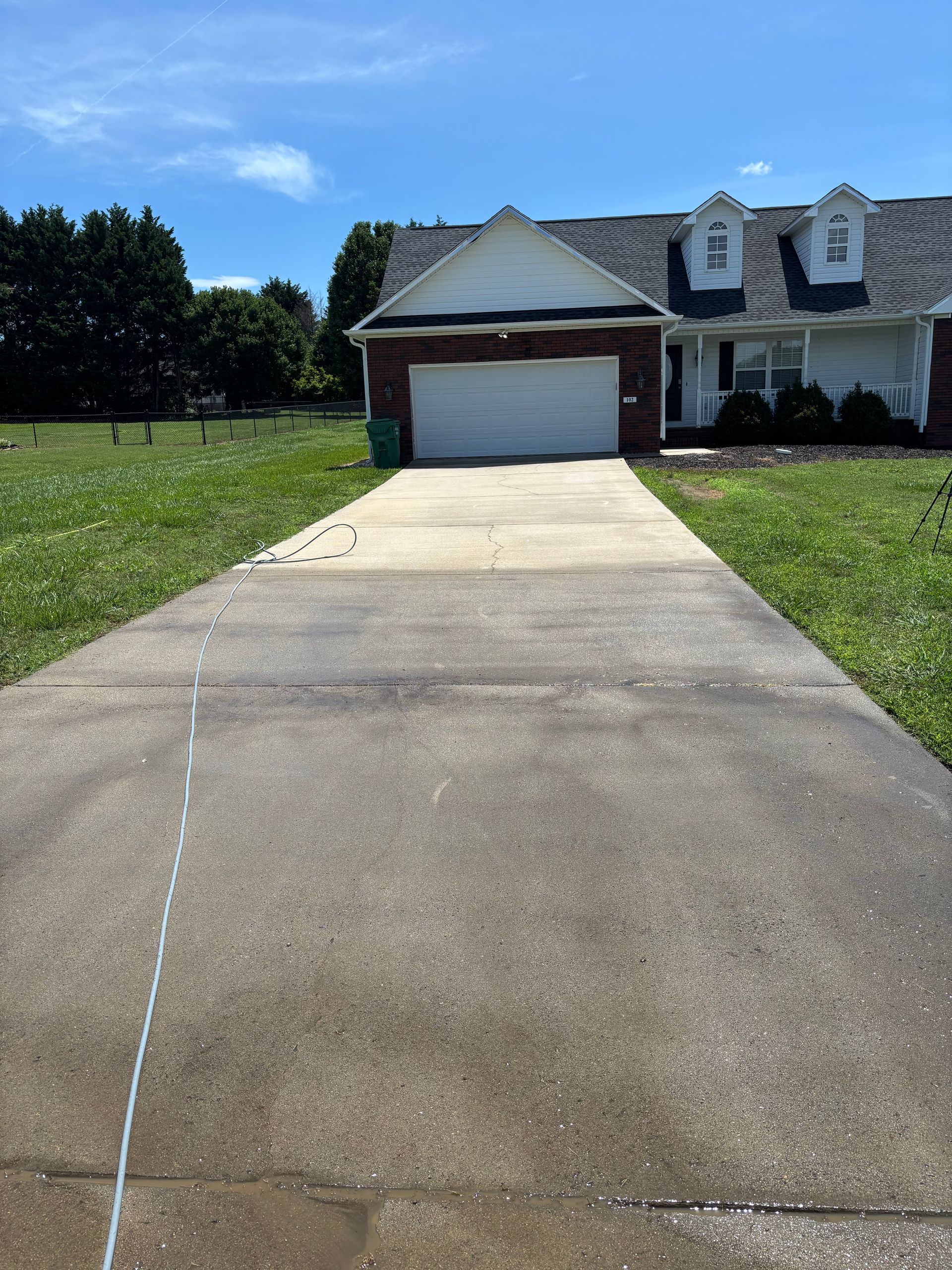 Concrete driveway leading to a brick house with a white garage door, under a blue sky.