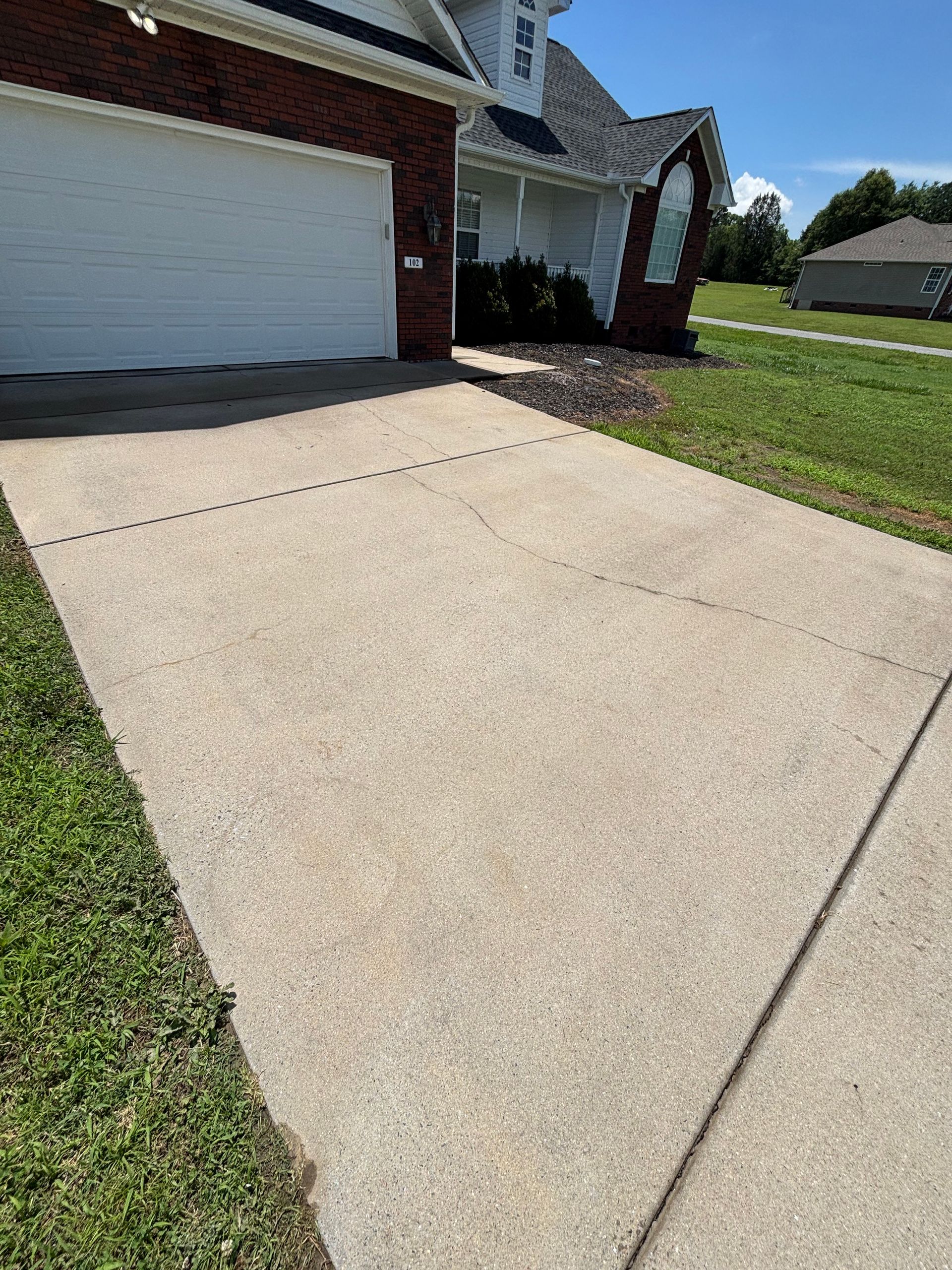 Concrete driveway leading to a brick-trimmed garage and white house on a sunny day.