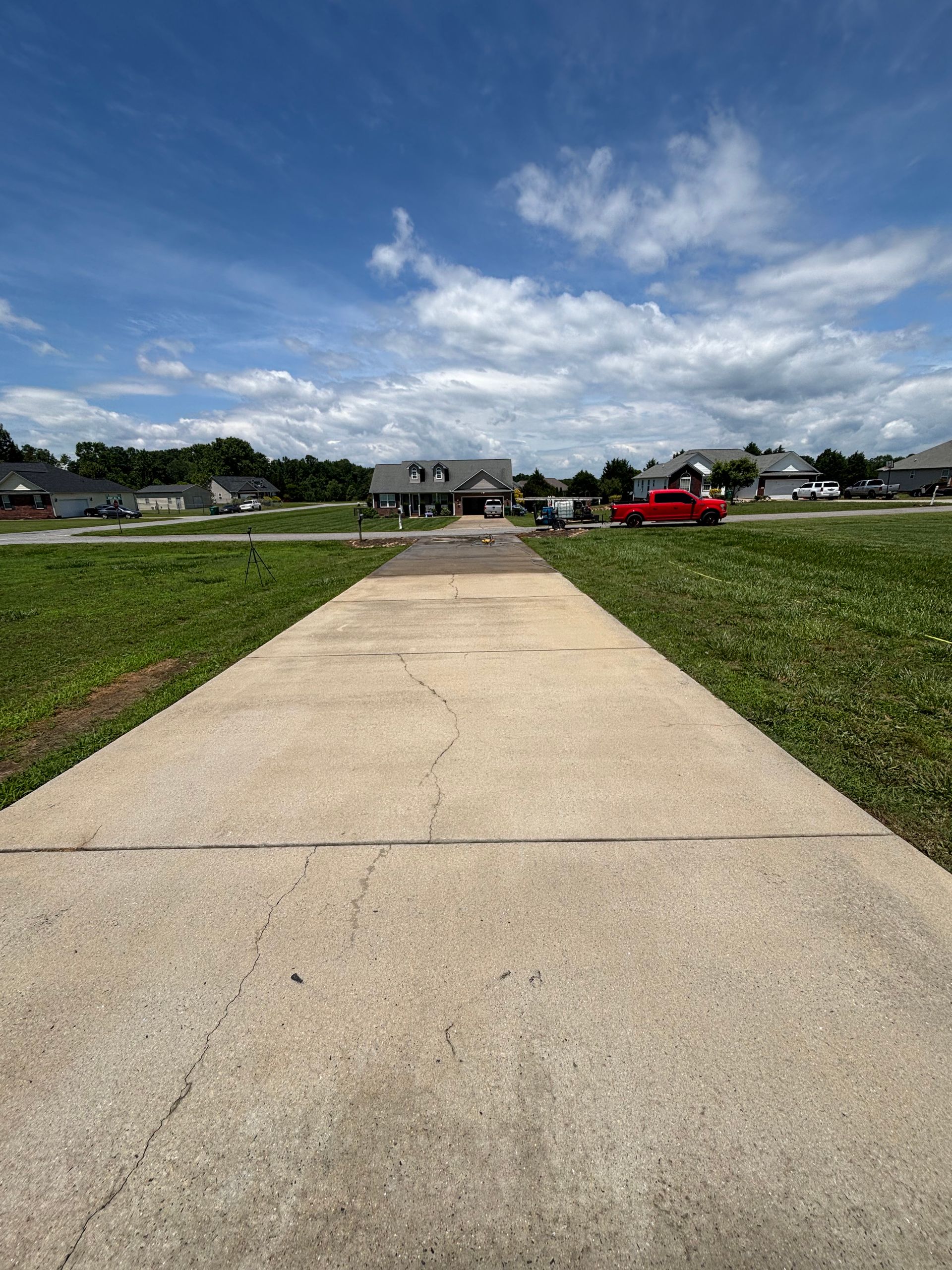 Concrete path leads to houses under blue sky with clouds. Grass on either side.