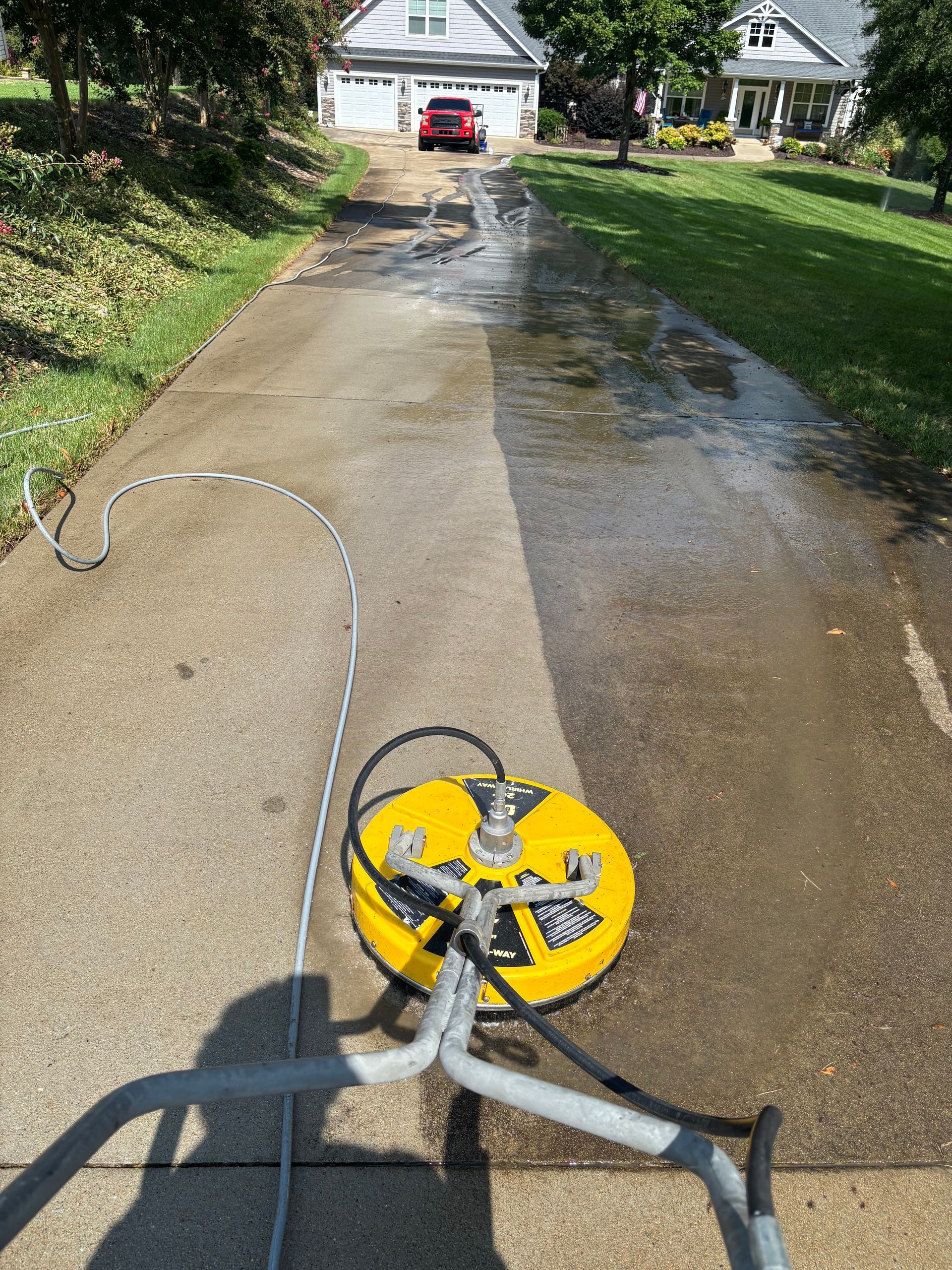 Pressure washer cleaning a driveway; half cleaned, half dirty; sunny day.
