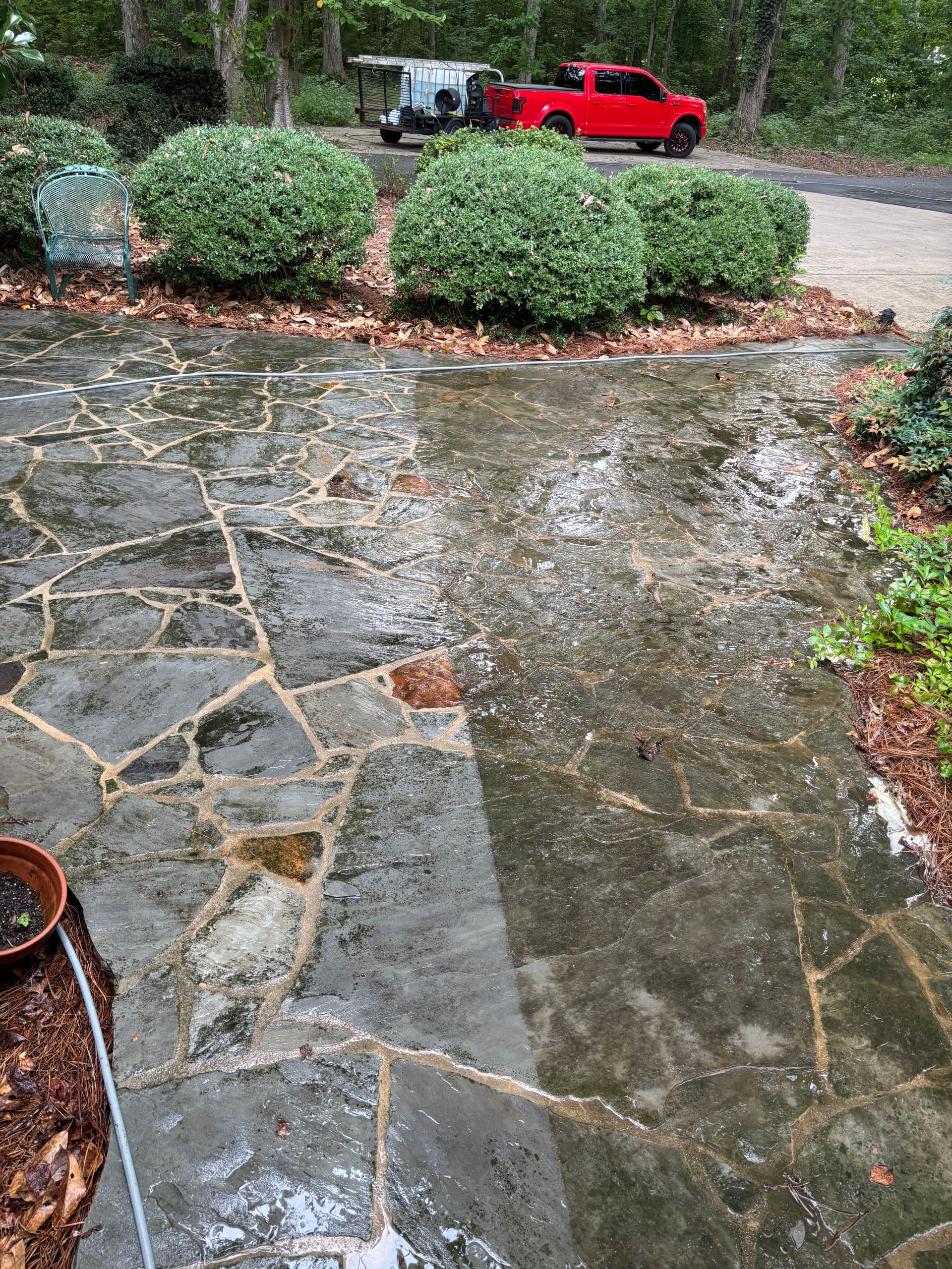 Wet stone patio with rain, green shrubs, red truck, and a trailer in the background.