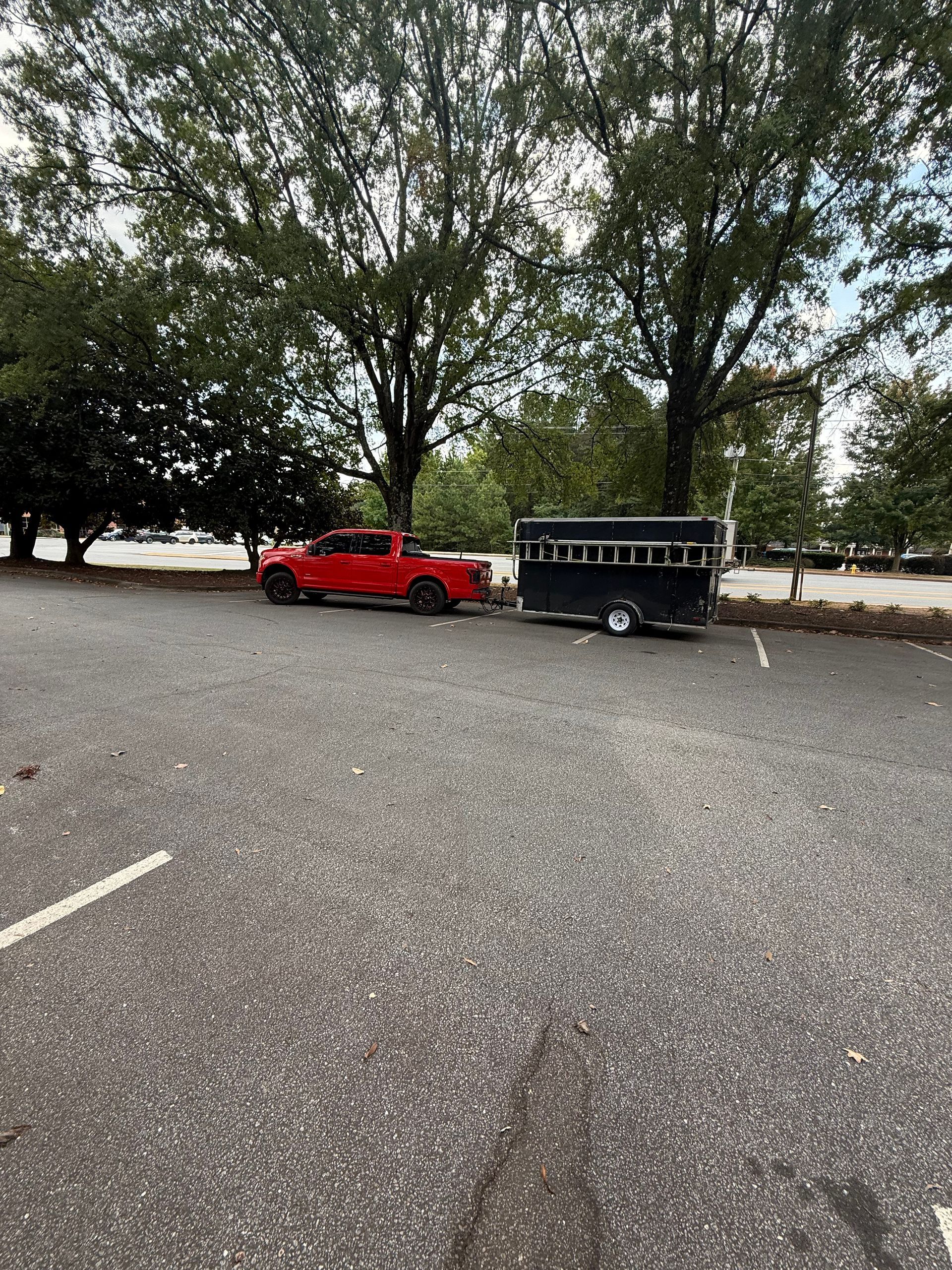 Red pickup truck towing a horse trailer in a paved parking lot lined with trees.