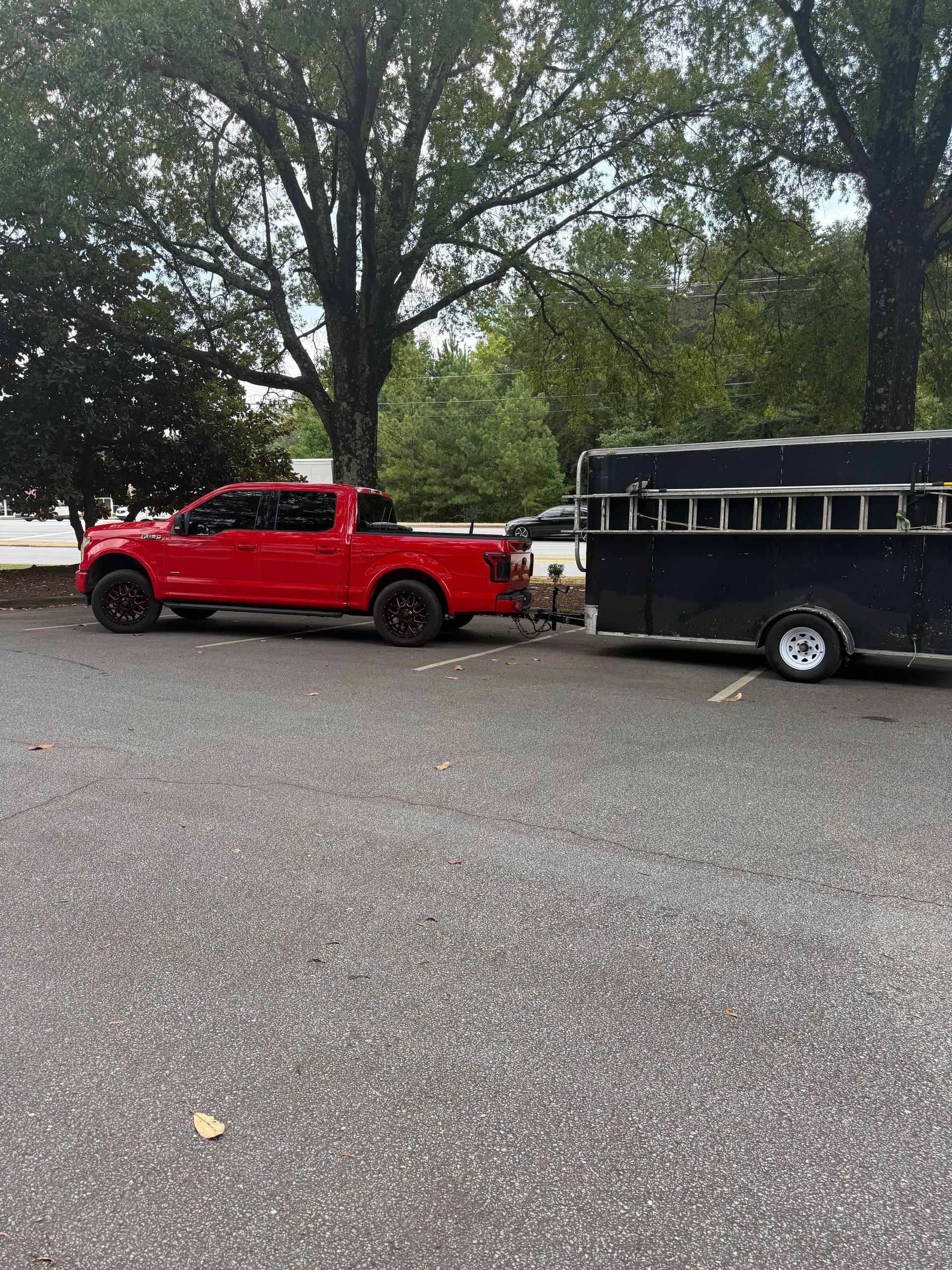 Red pickup truck towing a black horse trailer parked on asphalt.