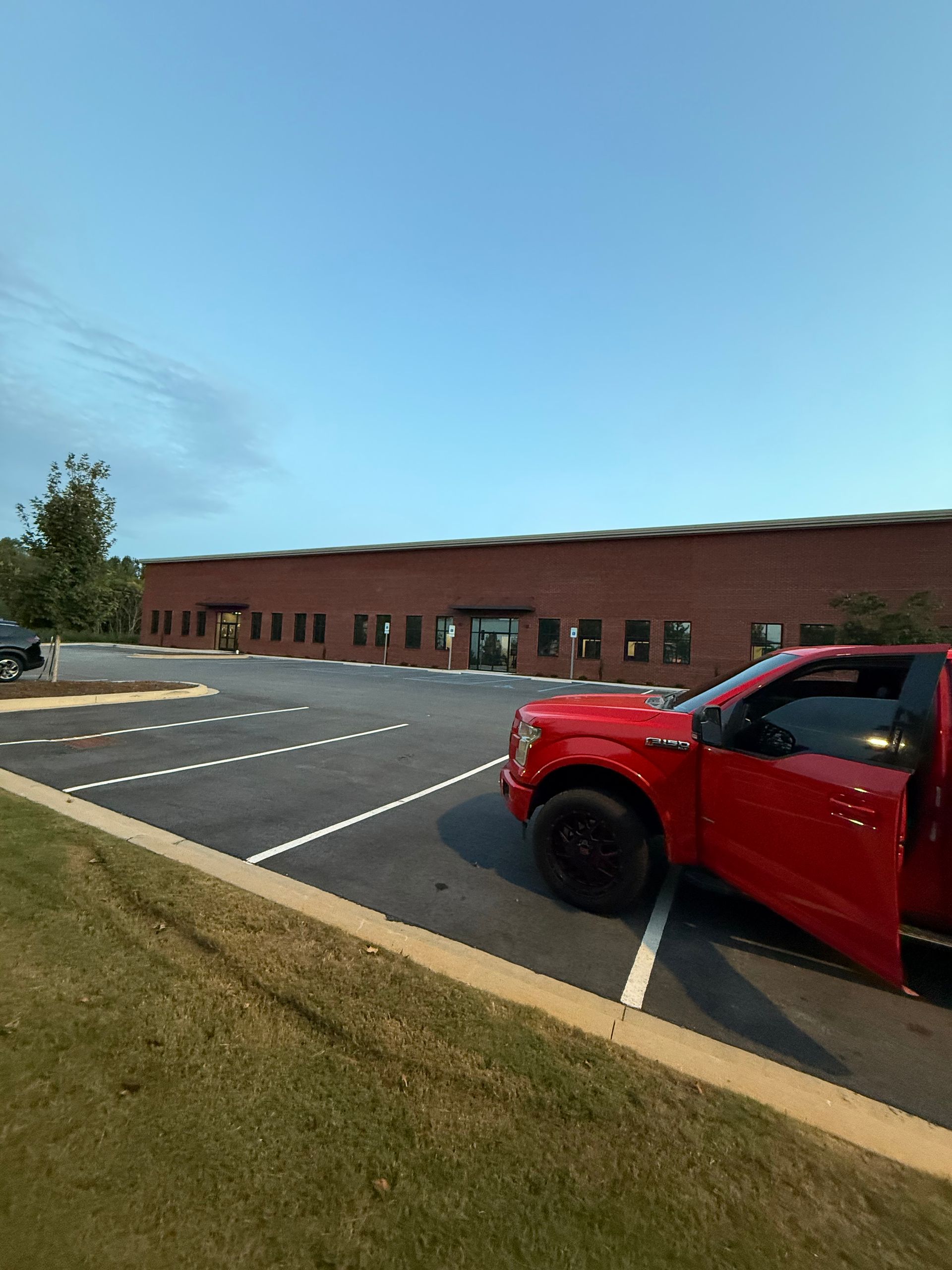 Red pickup truck parked outside a brick building with empty parking spaces under a blue sky.