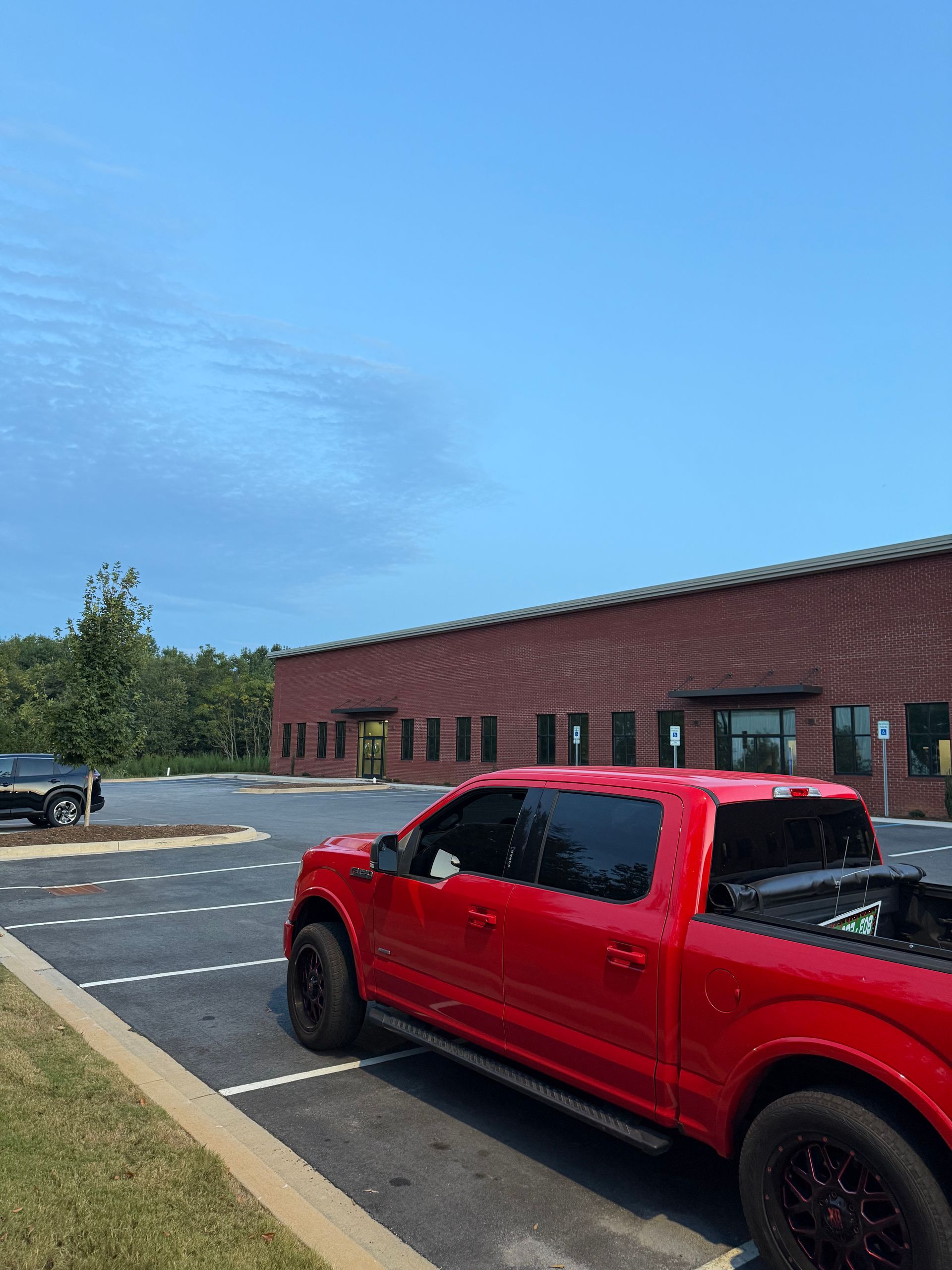 Red pickup truck parked outside a brick building on a sunny day.