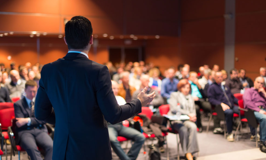 Man in suit giving presentation to an audience in a conference hall.