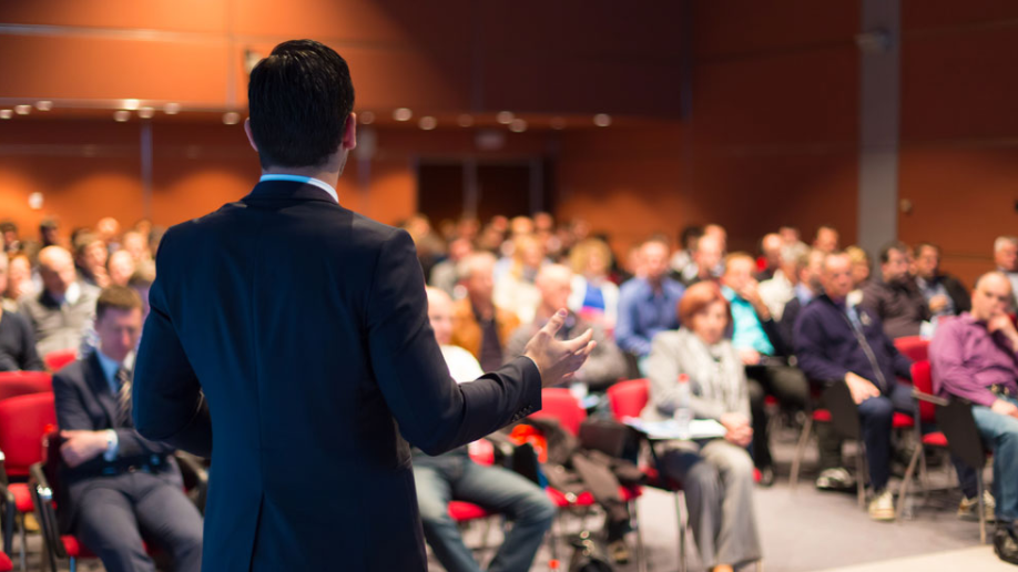 A man is giving a presentation to a large group of people in a conference room.