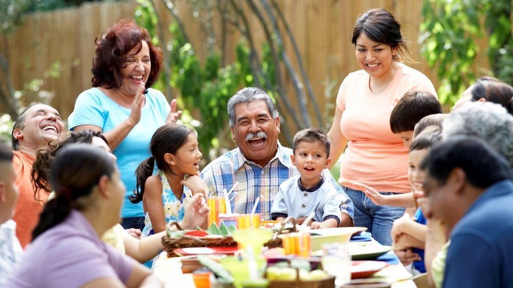 A large family is sitting at a table eating food.