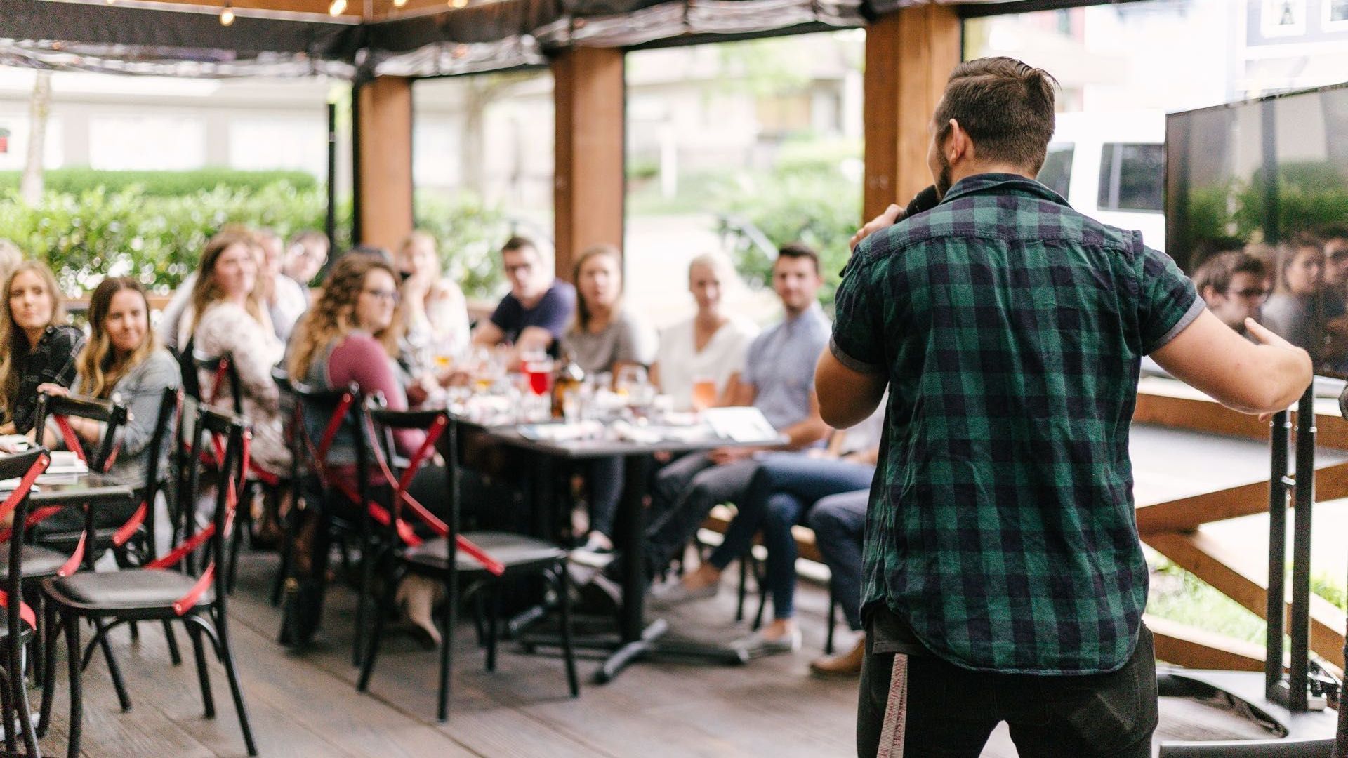 A man is giving a presentation to a group of people sitting at tables in a restaurant.